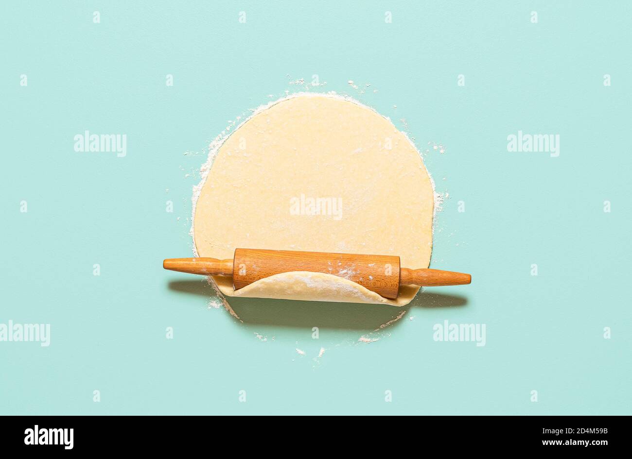 Concetto di cottura a casa con pasta cruda arrotolata con una spilla, isolata su sfondo verde-menta. Vista dall'alto della crosta di torta fatta in casa sul tavolo. Foto Stock