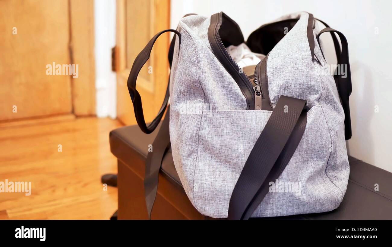 borsa da palestra in borsone grigio per lo sport e il fitness, una borsa aperta senza marchio piena di vestiti sul tavolo con sfondo della stanza e spazio per la copia. Foto Stock