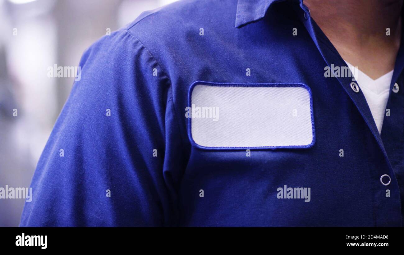 Uomo irriconoscibile che indossa una camicia blu uniforme con etichetta bianca vuota del nome o cerotto, identificazione del lavoratore o del dipendente. Foto Stock