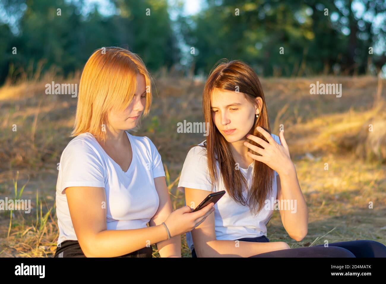 Due fidanzate guardano il telefono nel parco. Giovani belle donne nei social network sullo smartphone all'aperto in autunno. Foto Stock