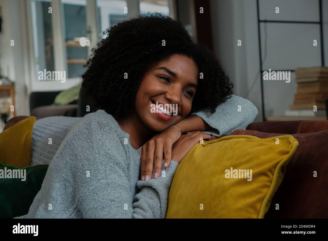Misto razza femminile pensare di nuovo a buoni ricordi mentre si siede sul divano a casa sorridendo Foto Stock