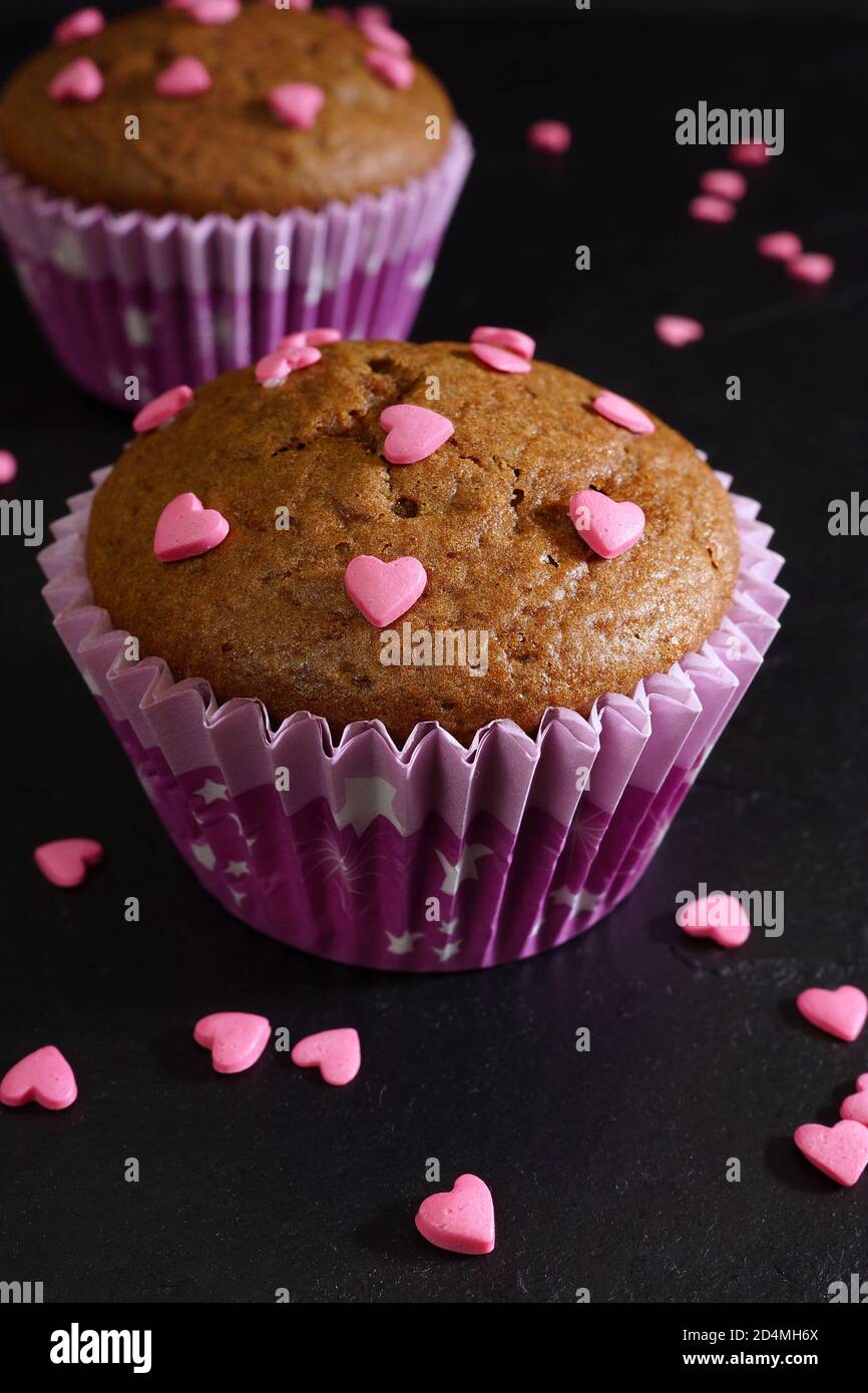 Muffin al cioccolato decorati con cuori di zucchero rosa. Sfondo nero. Primo piano Foto Stock