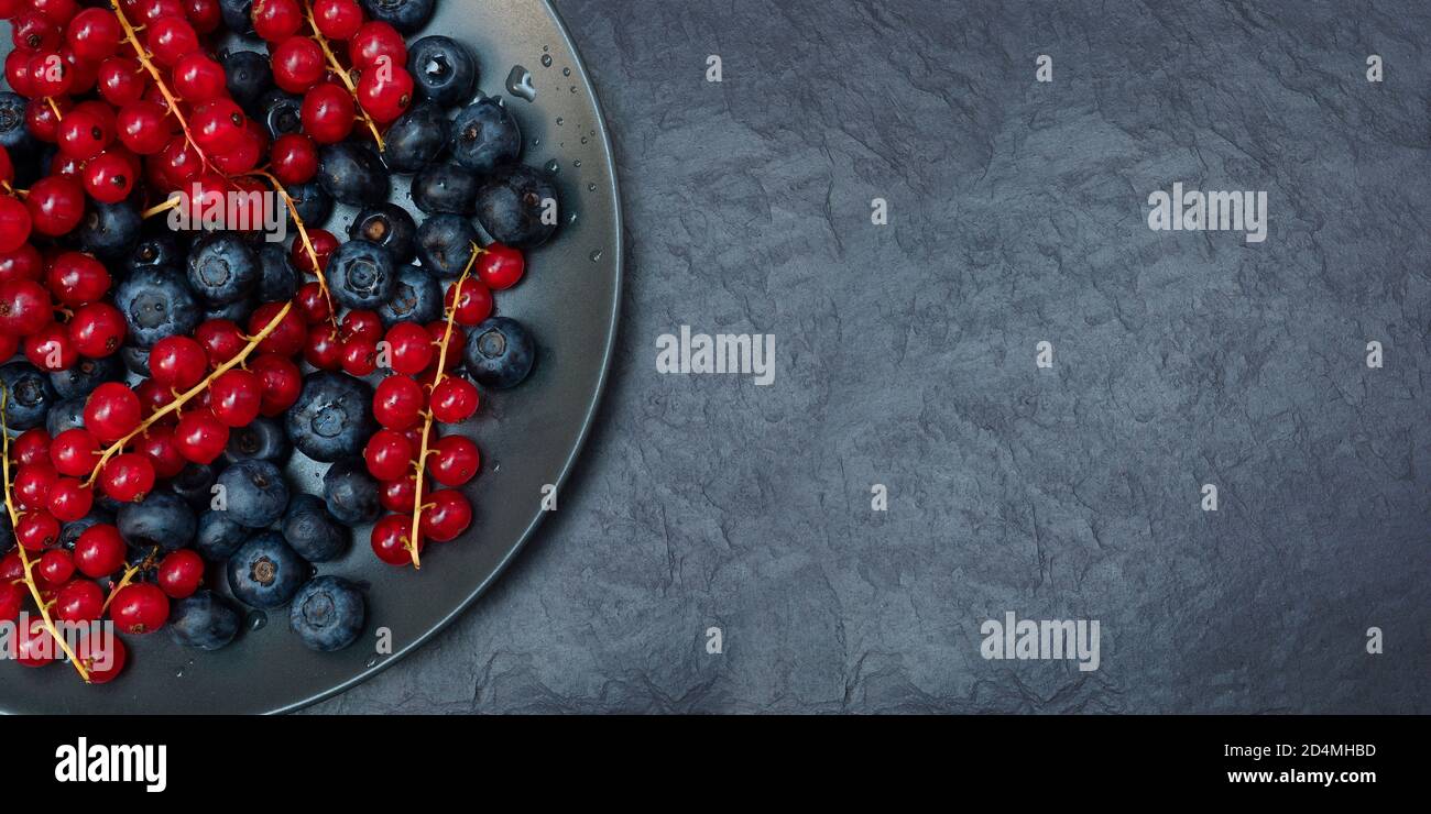 Bacche in un piatto nero. Ribes e mirtilli su un tavolo di ardesia nera. Vista dall'alto. Posiziona per il testo Foto Stock