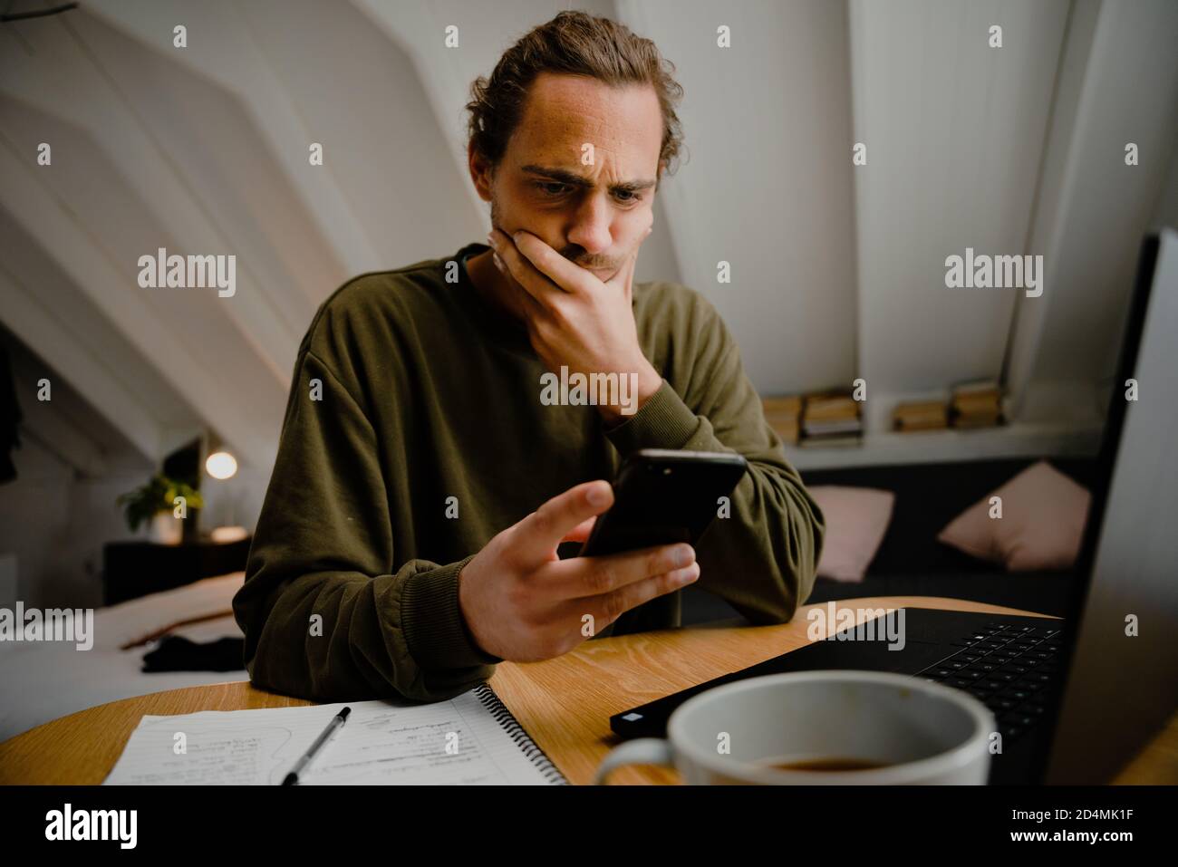 Giovane uomo creativo che lavora da casa, ricevendo messaggi di testo, confuso e incerto Foto Stock