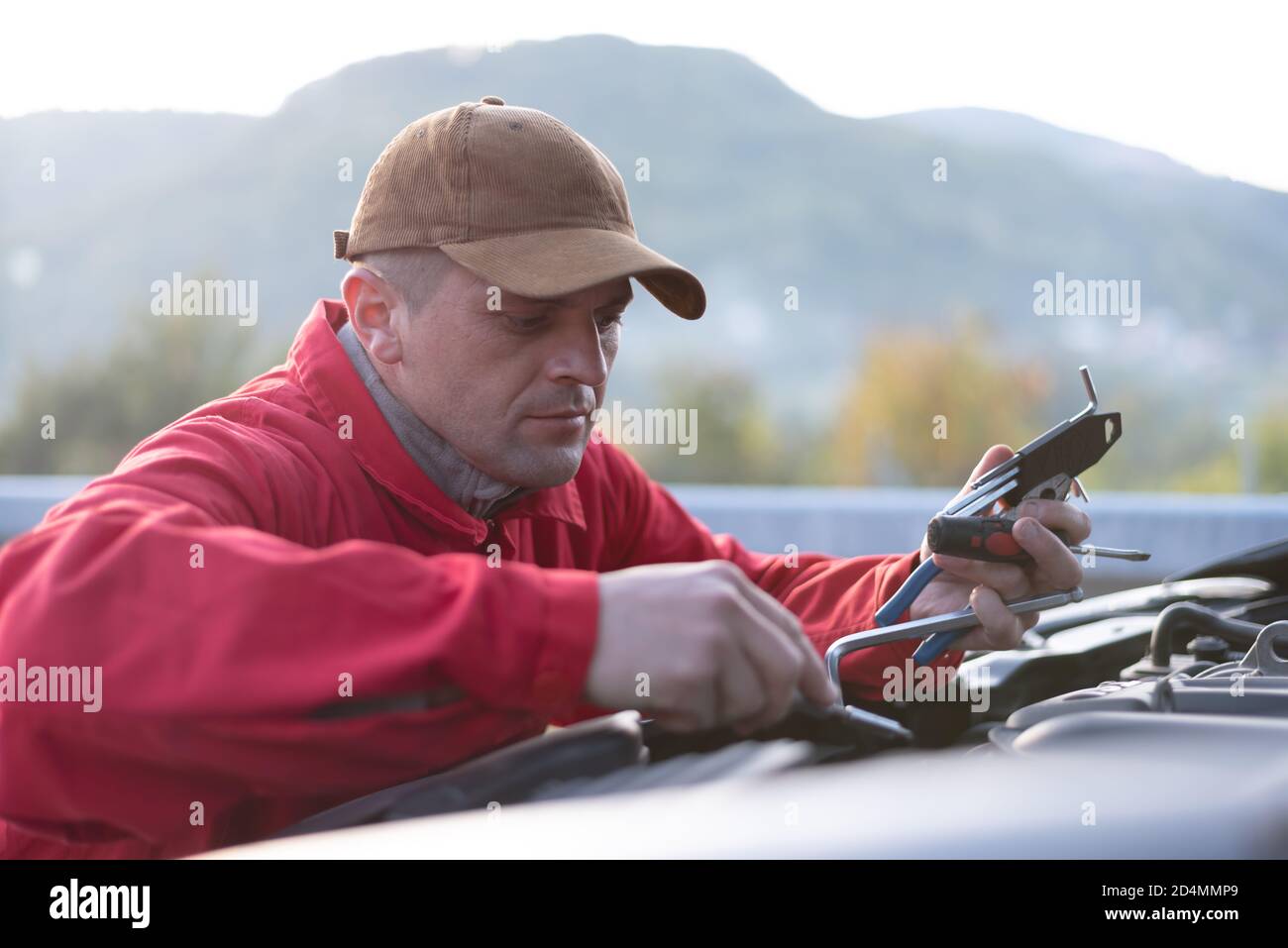 Assistenza stradale di emergenza, operatore di assistenza stradale in uniforme cercando di risolvere il guasto dell'auto o il guasto del motore. Concetto di assistenza stradale Foto Stock