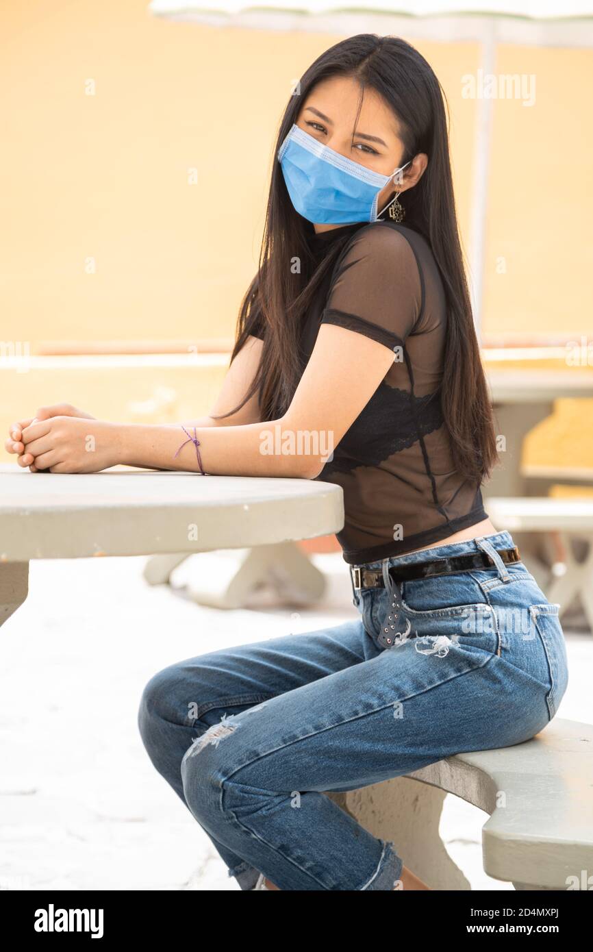 Giovane donna latina con lunghi capelli neri, seduta su un sedile accanto  ad un tavolo, indossando una blusa trasparente, jeans, giorno di sole Foto  stock - Alamy