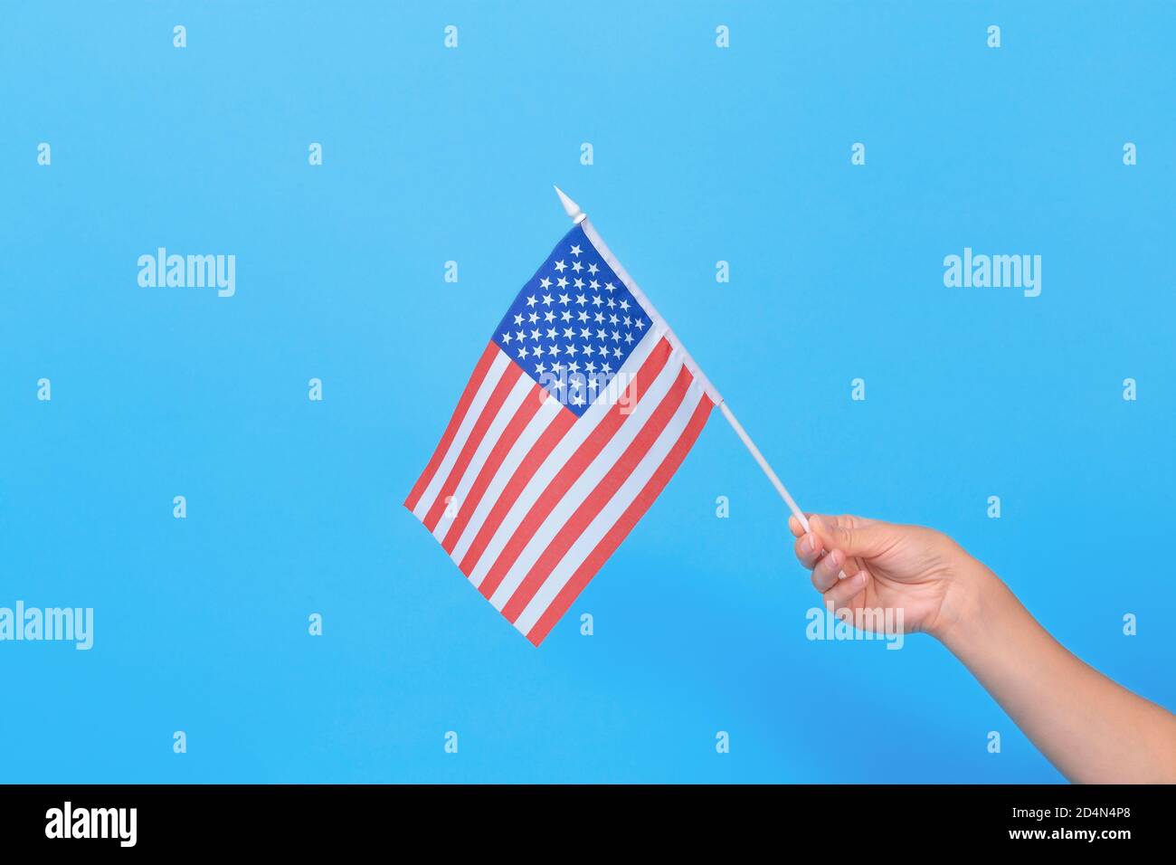 Mano di donna che tiene piccola bandiera americana su sfondo blu. Spazio per il testo. Foto Stock