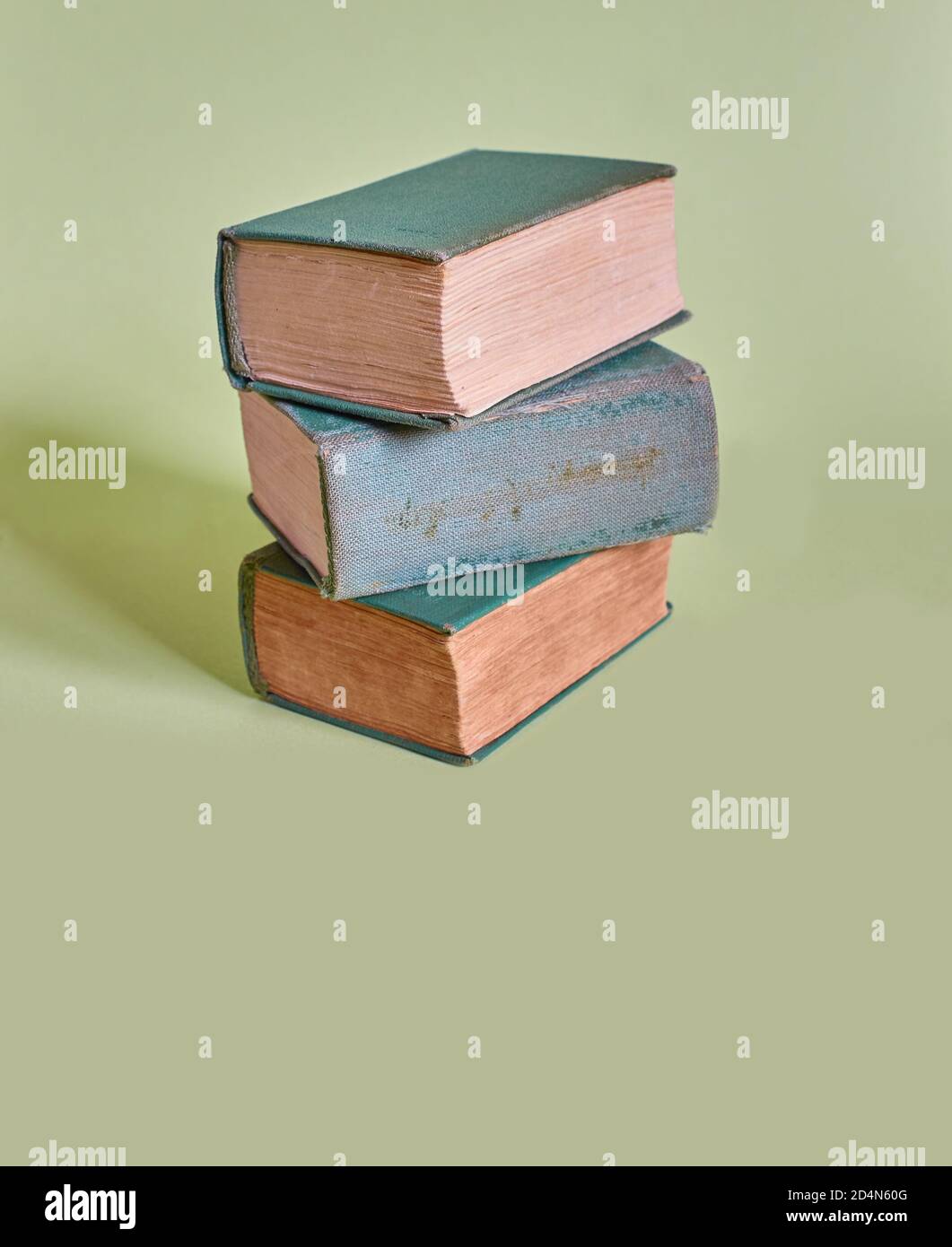 Una pila di tre vecchi libri si trova su uno sfondo verde chiaro. Formato verticale Foto Stock