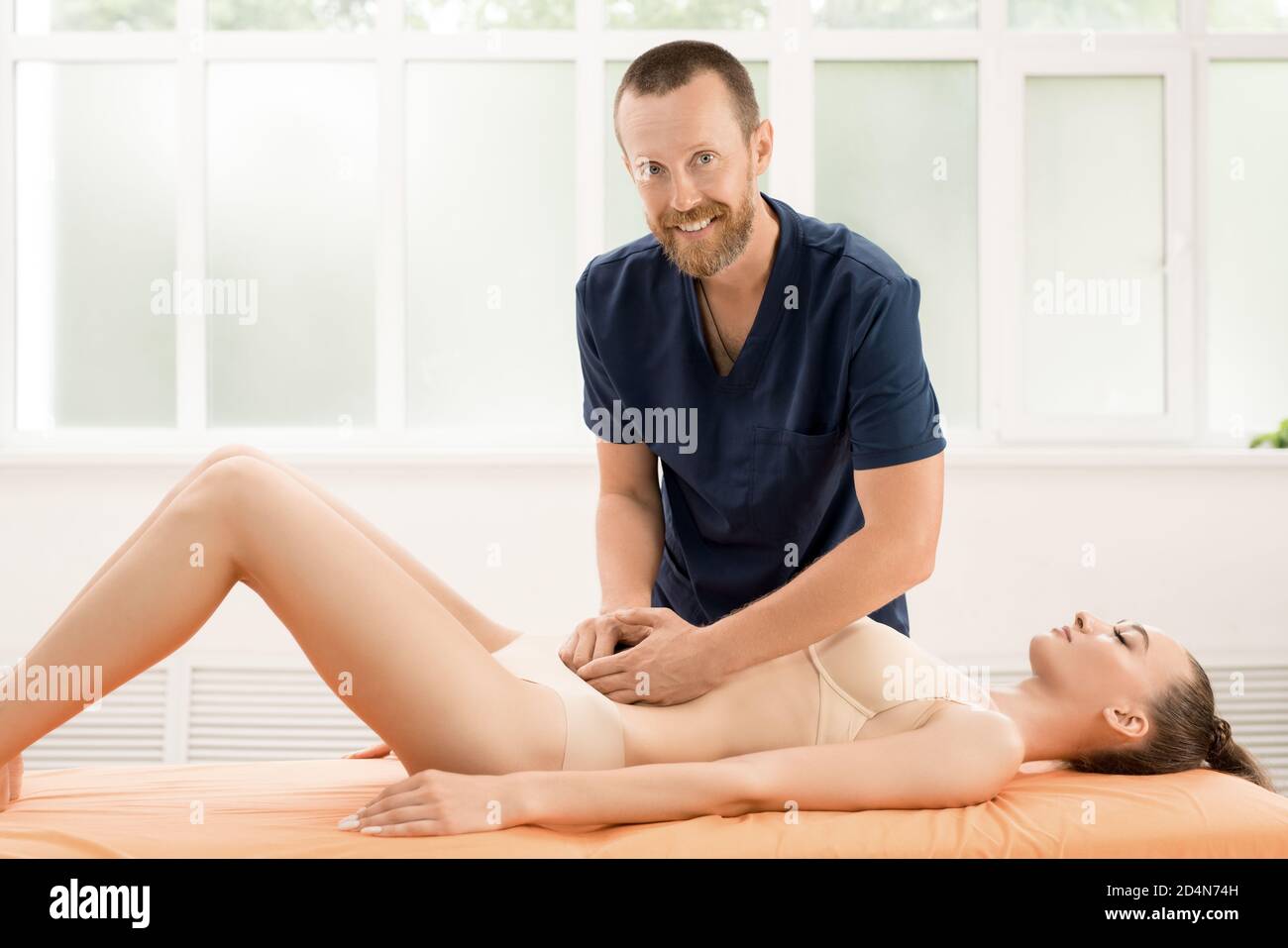 Ottimista terapeuta osteopatica maschile massaggiante addome femminile paziente durante il trattamento di problemi digestivi in clinica moderna Foto Stock