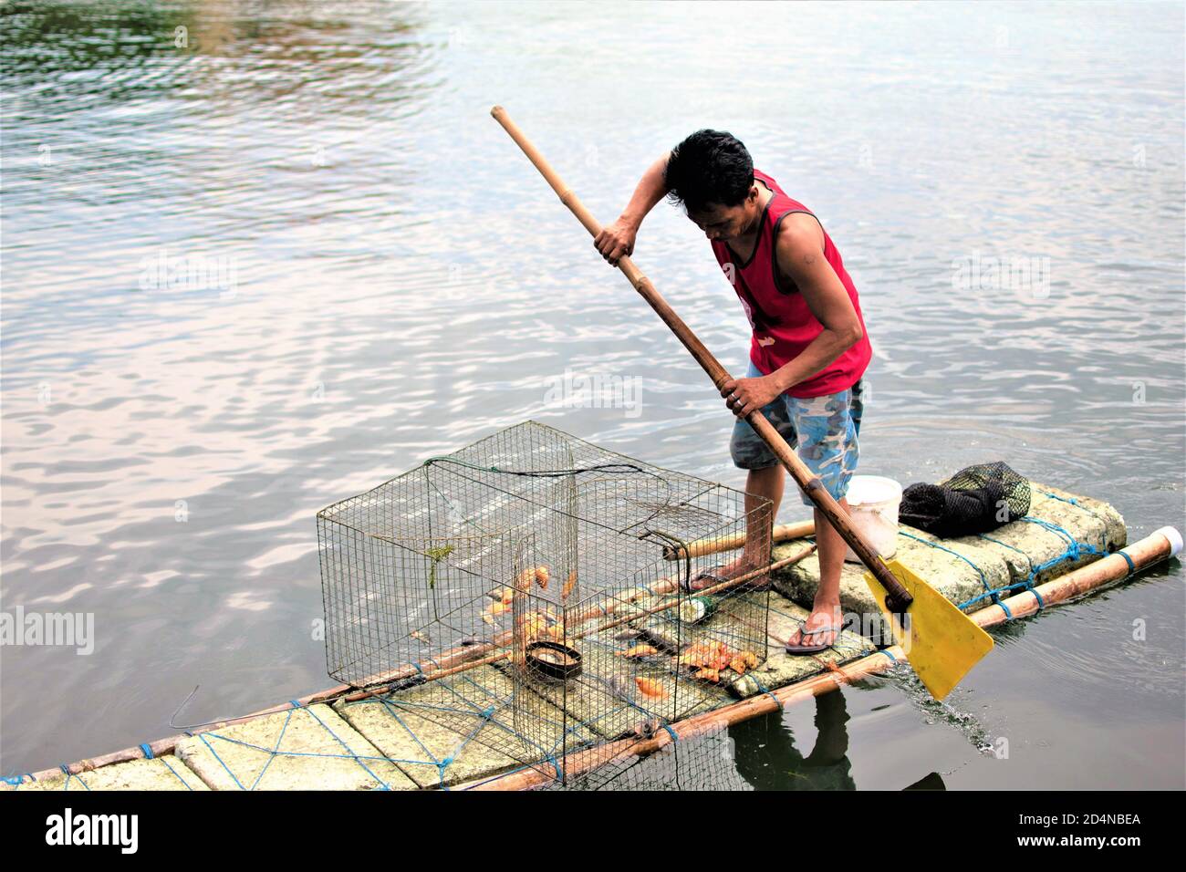 Un uomo cattura il pesce in un lago utilizzando un makeshift barca fatta di schiuma di plastica e pali di bambù Foto Stock