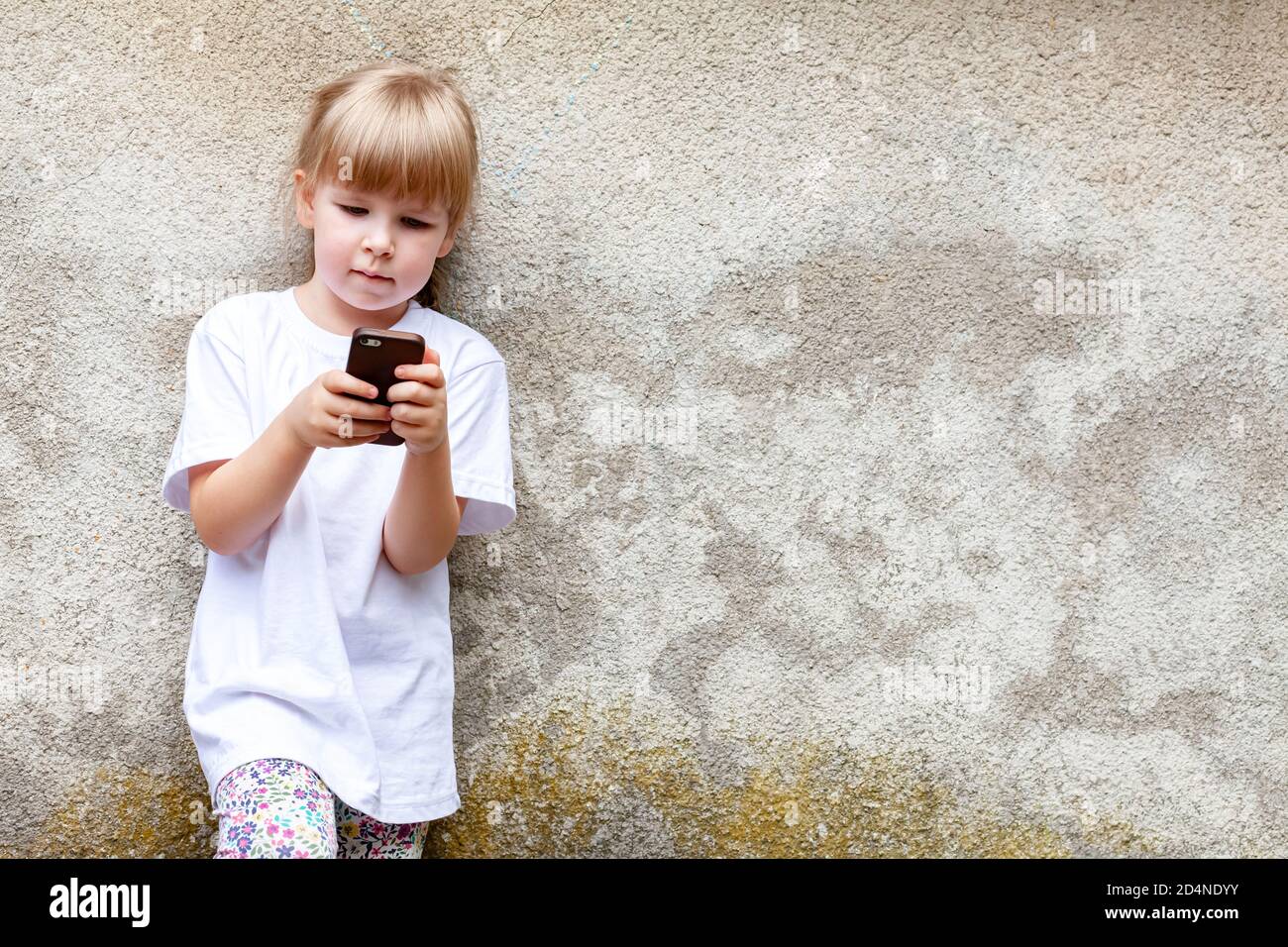 Bambina, bambino che usa uno smartphone moderno in piedi all'aperto. Capretto da solo ha messo a fuoco sul suo telefono mobile, copyspace. Bambini occupati con tecnologia Foto Stock