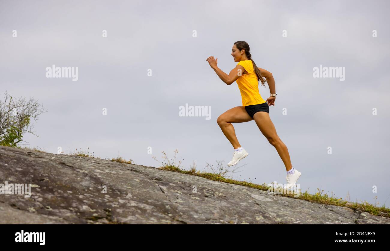 Vista laterale di una donna che fa una corsa ad alta intensità sul fianco della montagna vicino al mare Foto Stock