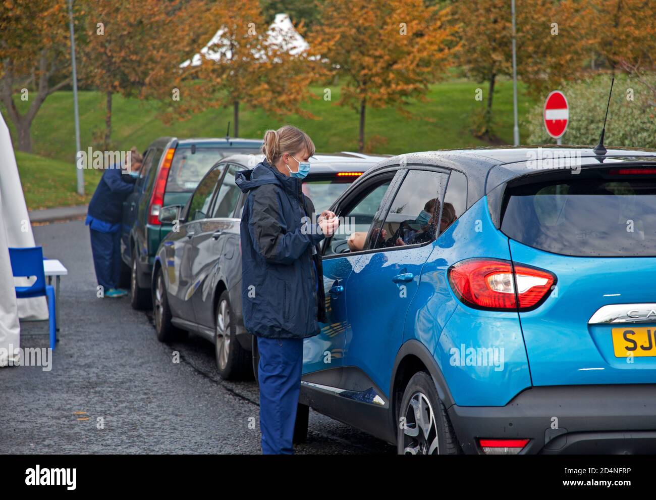 Holyrood High School, Edimburgo, Scozia, Regno Unito. 10 ottobre 2020. Guidare attraverso il Flu Jab Queue causa caos di traffico, come centinaia di auto parcheggiate in attesa in coda in Duddingston Road West, L'autobus locale 42 doveva essere diretto oltre la linea di traffico che si estende per tutta la lunghezza della strada e dietro l'angolo in Milton Road West. Questo continuerà per i prossimi 4 fine settimana dalle 9:00 alle 17:30. Nella foto: Il componente dello staff si prepara a vaccinare un conducente. Credit: Arch White/Alamy Live News. Foto Stock