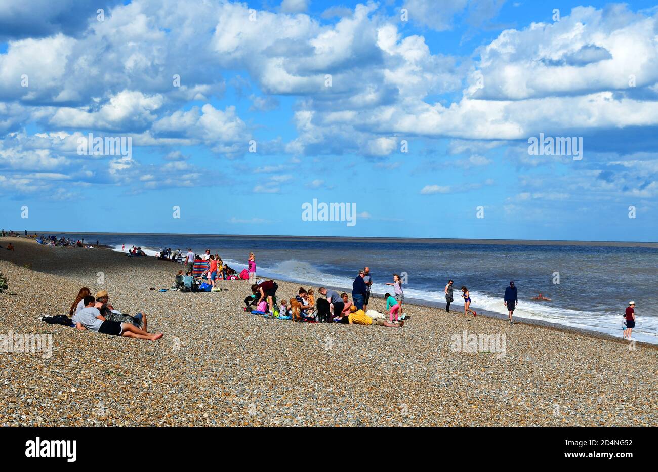 Le persone che si godono la spiaggia di ciottoli in una giornata di sole luminoso nel mese di agosto. Thorpeness, Suffolk, Regno Unito Foto Stock