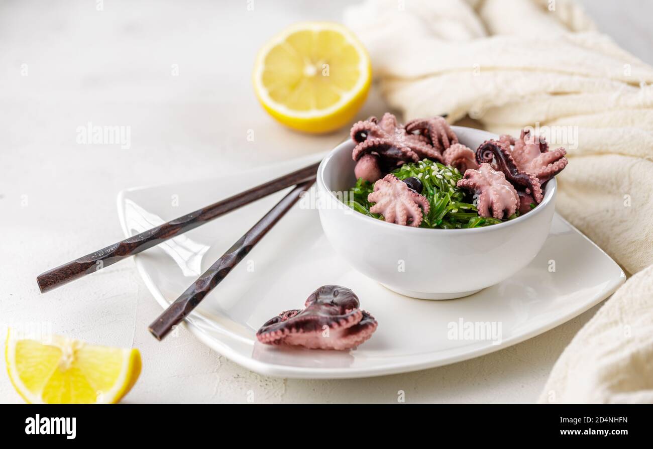 Foto ritagliata di insalata verde di alghe di wakame con semi di sesamo e mini polpo serviti con chopstick al ristorante Foto Stock
