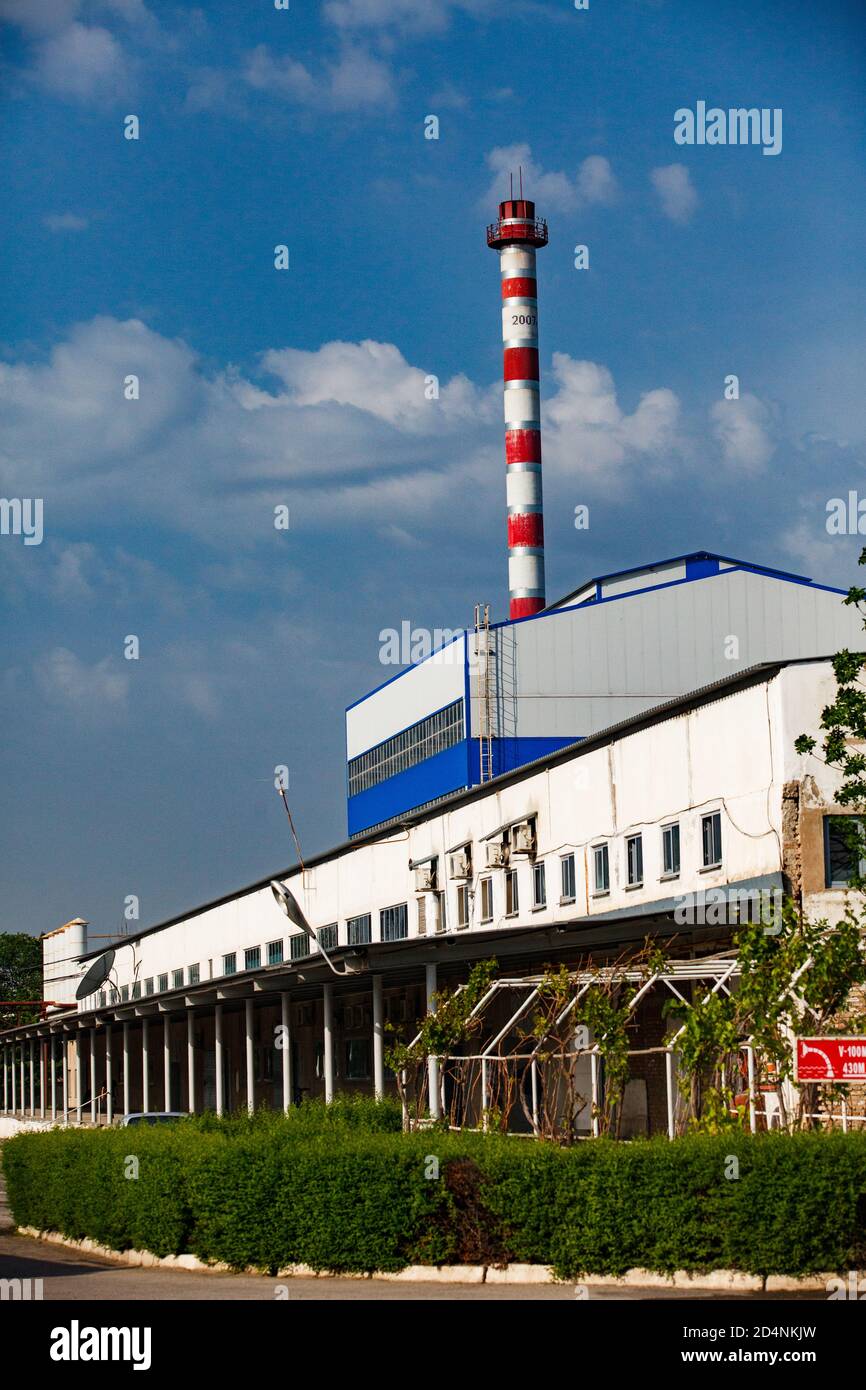 Fabbrica di vetro Darkhan. Centrale elettrica a gas, camino a strisce rosso e bianco e costruzione industriale. Cielo blu, nuvole. Città di Shymkent, Kazakistan Foto Stock