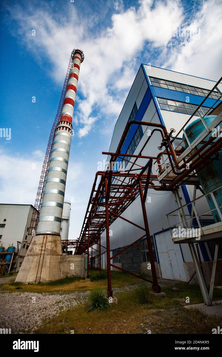 Fabbrica di vetro Darkhan, Shymkent, Kazakhstan. Centrale elettrica a gas, camino a strisce rosso e bianco e costruzione industriale. Cielo blu con nuvole. Foto Stock