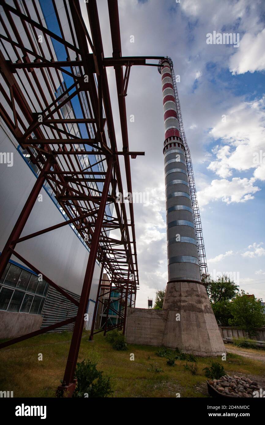 Fabbrica di vetro Darkhan, Shymkent, Kazakhstan. Centrale elettrica a gas, camino a strisce rosso e bianco e costruzione industriale. Cielo blu, nuvole. Foto Stock