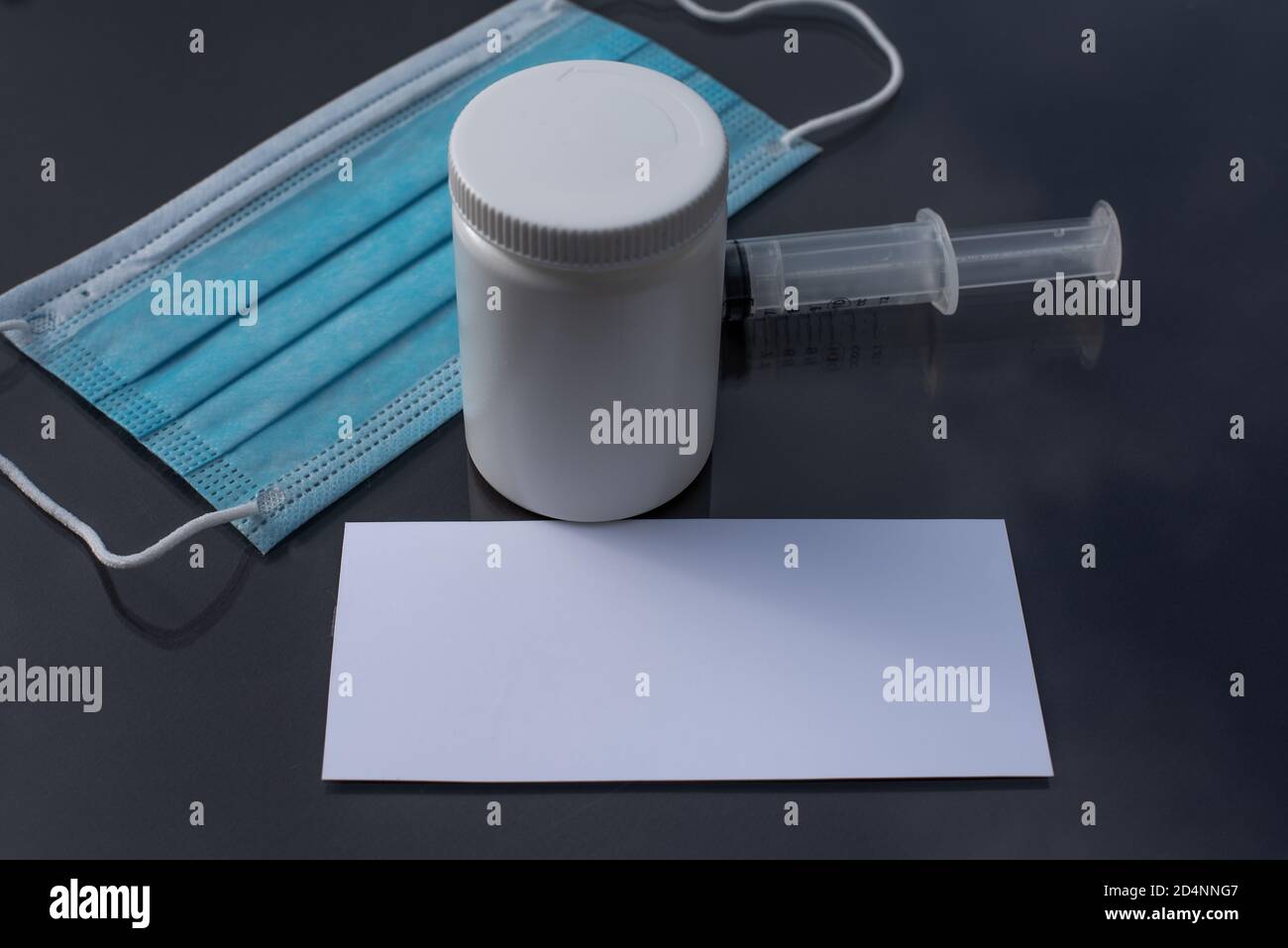 Spazio per il testo su un foglio di carta bianco su una scrivania nera con una siringa e una maschera facciale per la protezione contro covid-19, Danimarca, ottobre 10,2020 Foto Stock