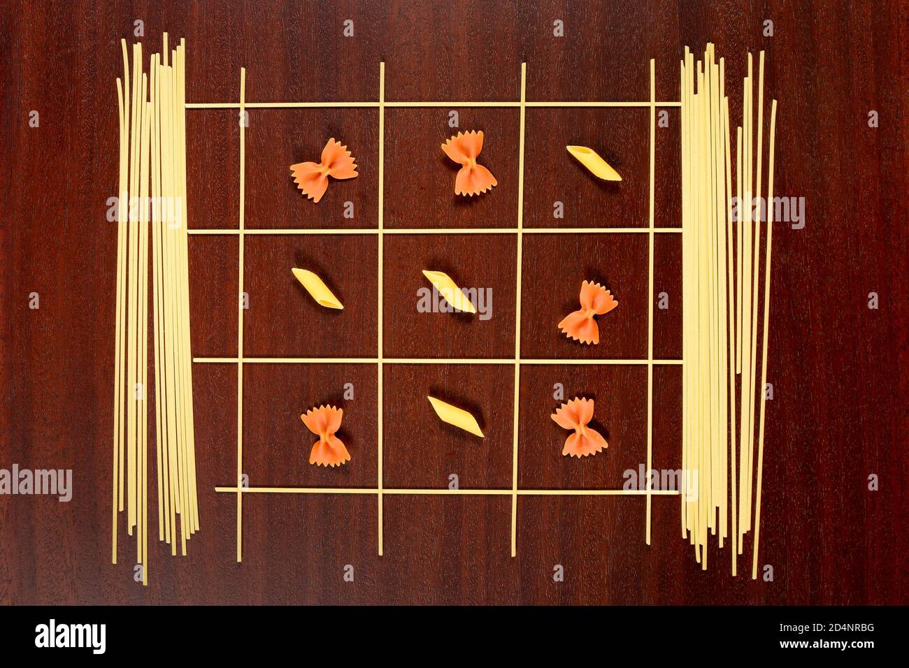 Pasta italiana. TIC TAC Toe o Xs e OS gioco fatto da spaghetti crudi, farfalle rosso e penne gialle. Asciugare i maccheroni e i capellini su un tavolo di legno marrone. Foto Stock