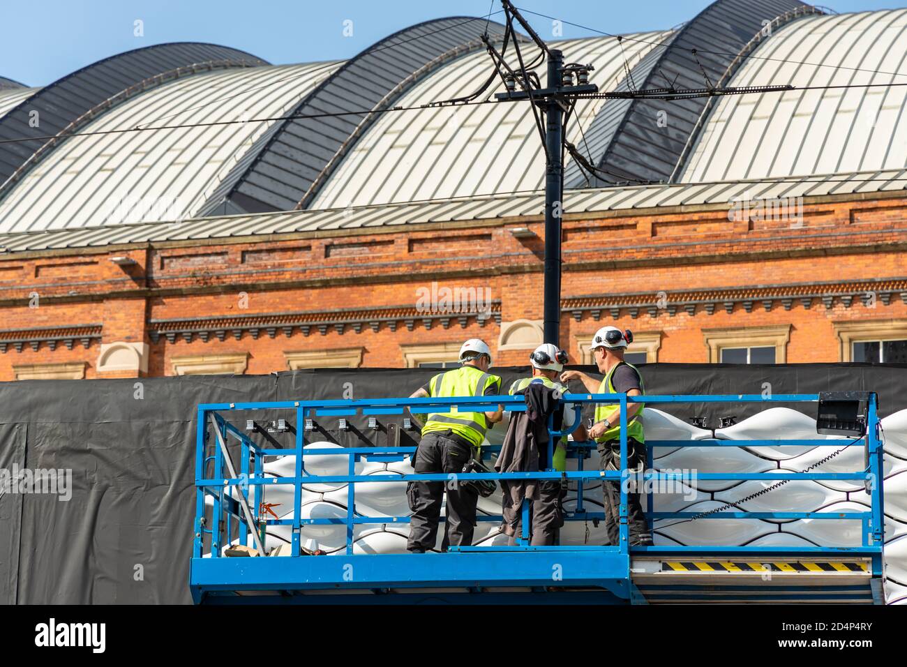 Tre operai edili su una piattaforma che ispezionano le piastrelle in ceramica nel centro di Manchester, parte della struttura di pizzo conchiglia. Foto Stock