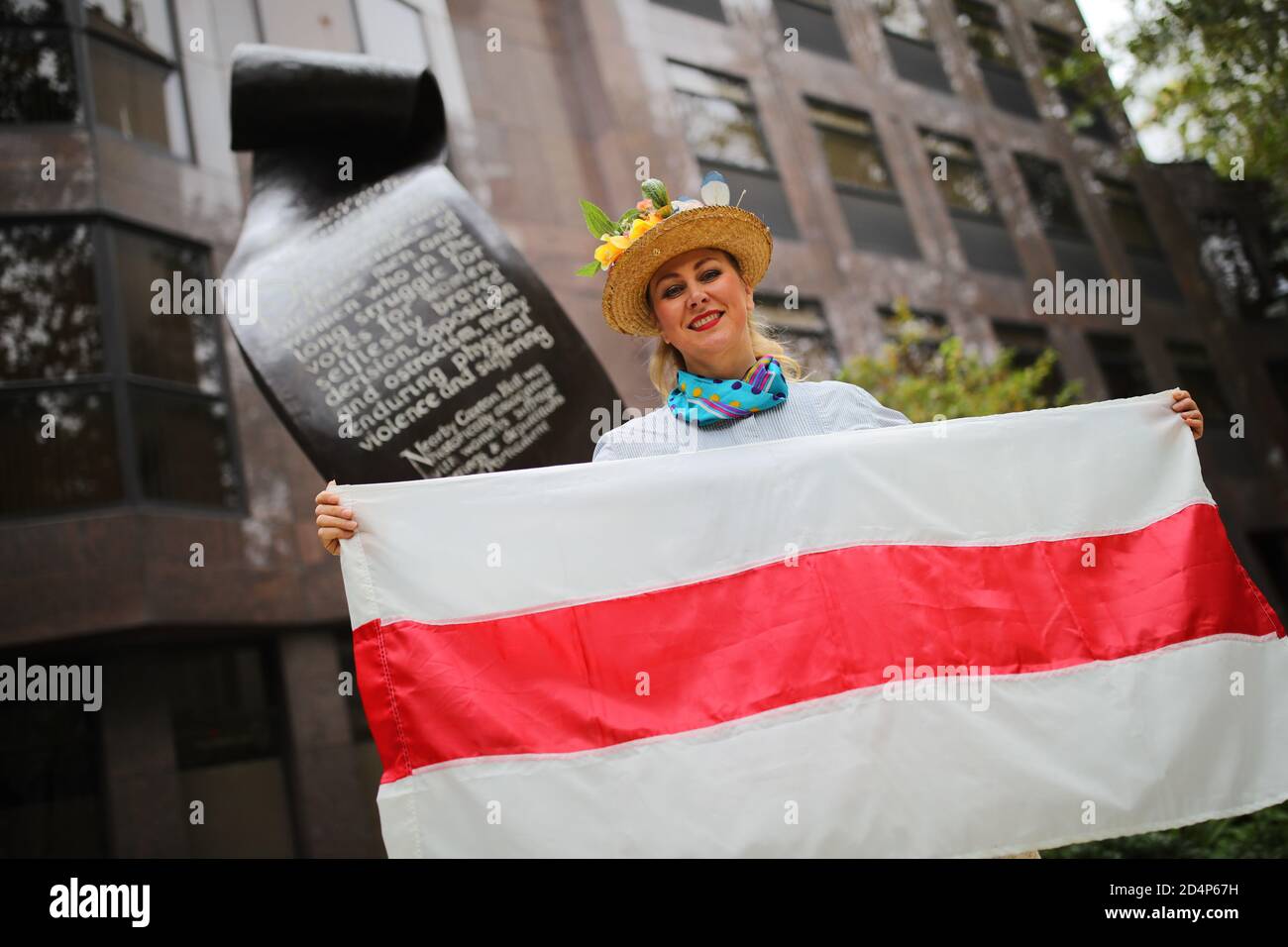 Una donna in piedi davanti al Suffragette Memorial a Victoria, Londra, che detiene una bandiera storica di uno stato bielorusso indipendente, dopo la rottura dell'impero russo, prima di marciare in solidarita con le donne della Bielorussia a Downing Street, Londra. Foto Stock