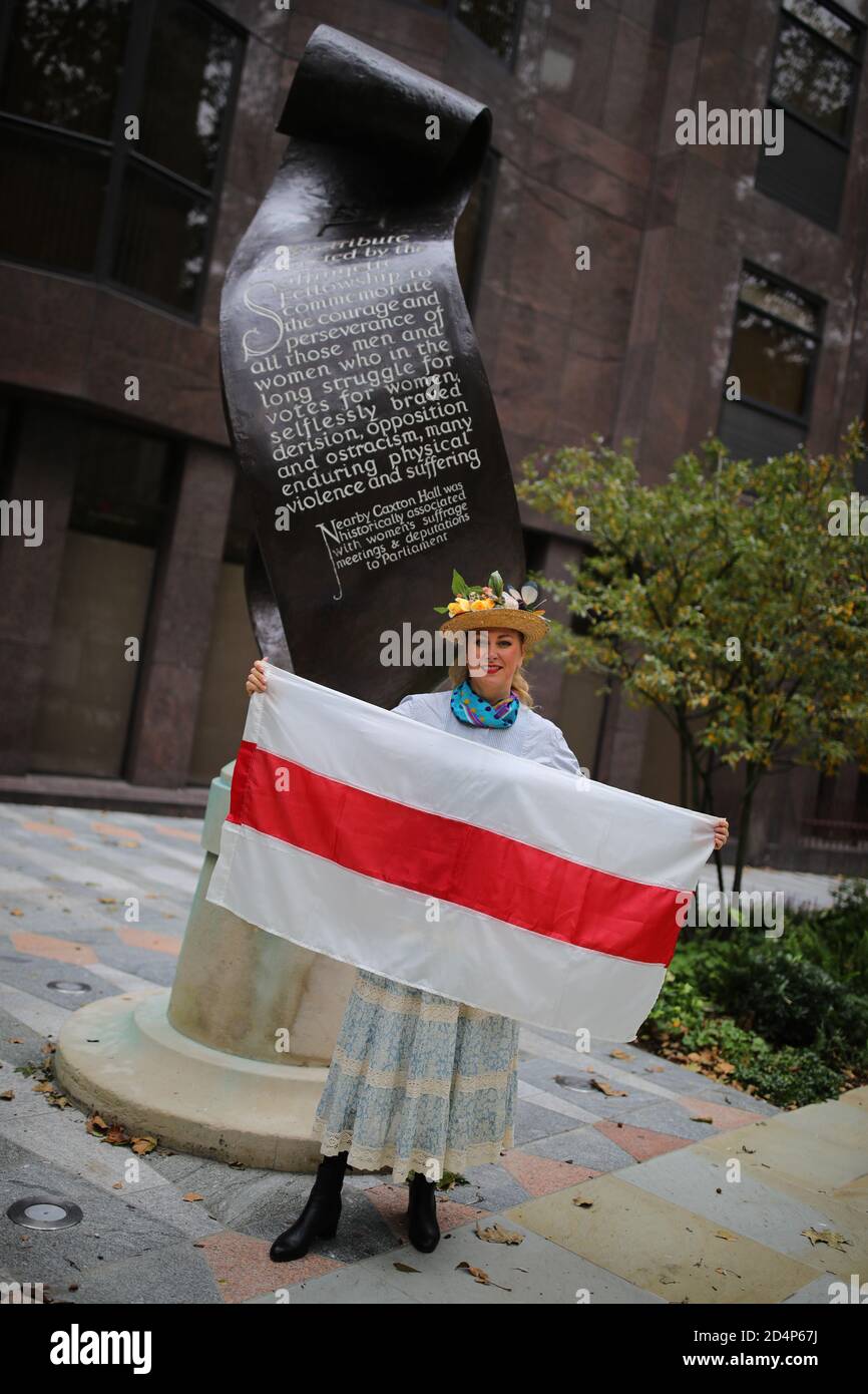Una donna in piedi davanti al Suffragette Memorial a Victoria, Londra, che detiene una bandiera storica di uno stato bielorusso indipendente, dopo la rottura dell'impero russo, prima di marciare in solidarita con le donne della Bielorussia a Downing Street, Londra. Foto Stock