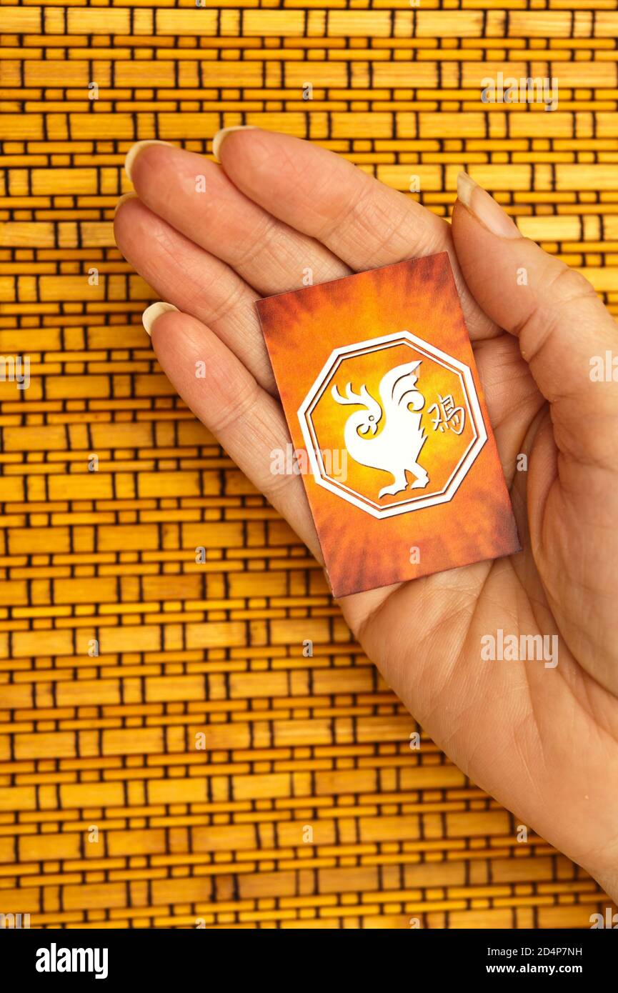 Mano che tiene una carta del segno cinese dell'oroscopo Gallo Foto Stock