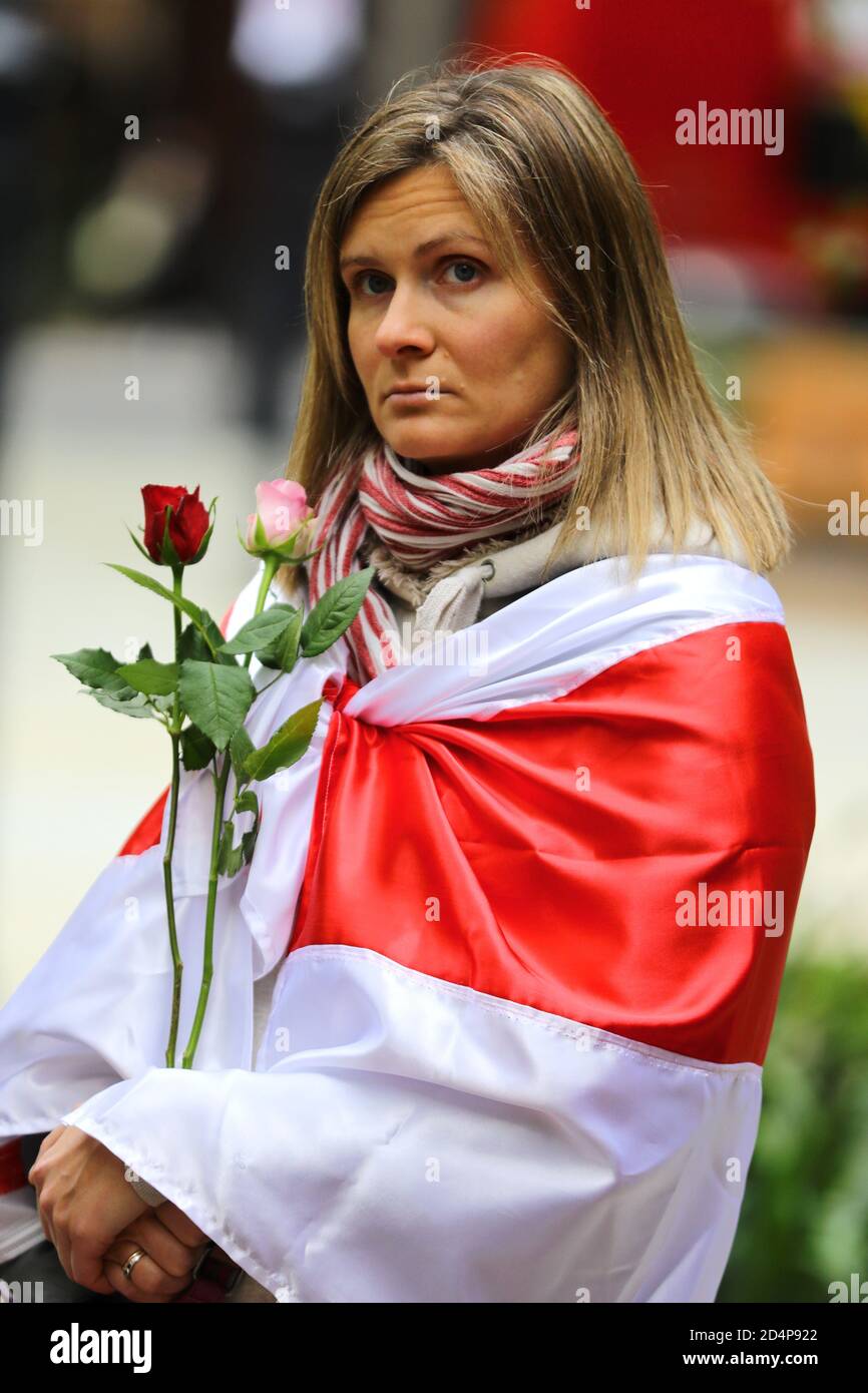 Una donna che tiene rose, avvolta in una bandiera storica di uno stato bielorusso indipendente, dopo la rottura dell'impero russo, si prepara a marzo, in solidarietà con le donne bielorusse, dal Monumento Suffragette a Downing Street, Londra. Foto Stock