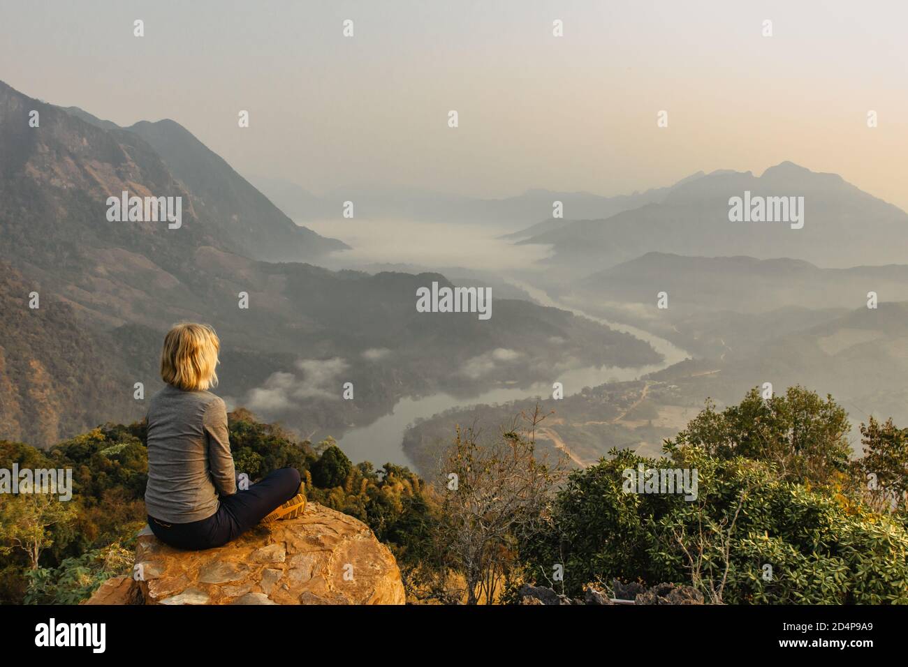 Rilassati dopo l'escursione mattutina fino alla vetta del mountain.Female viaggiatore seduto su una roccia in Laos.Sunrise watching.Amazing vista di un fiume, montagne Foto Stock