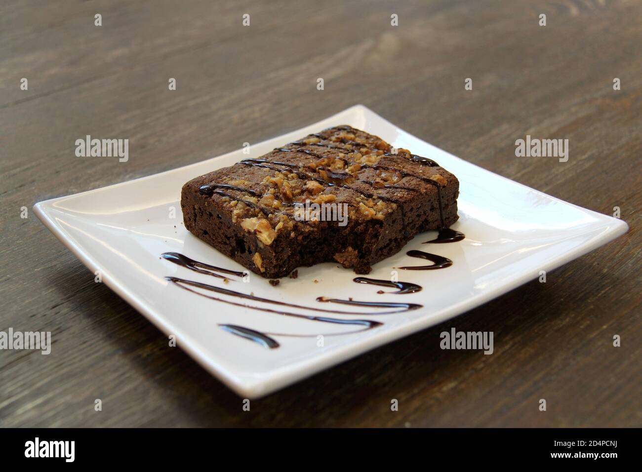 Un pezzo di brownie in un piatto con salsa al cioccolato e noci tritate. Foto Stock