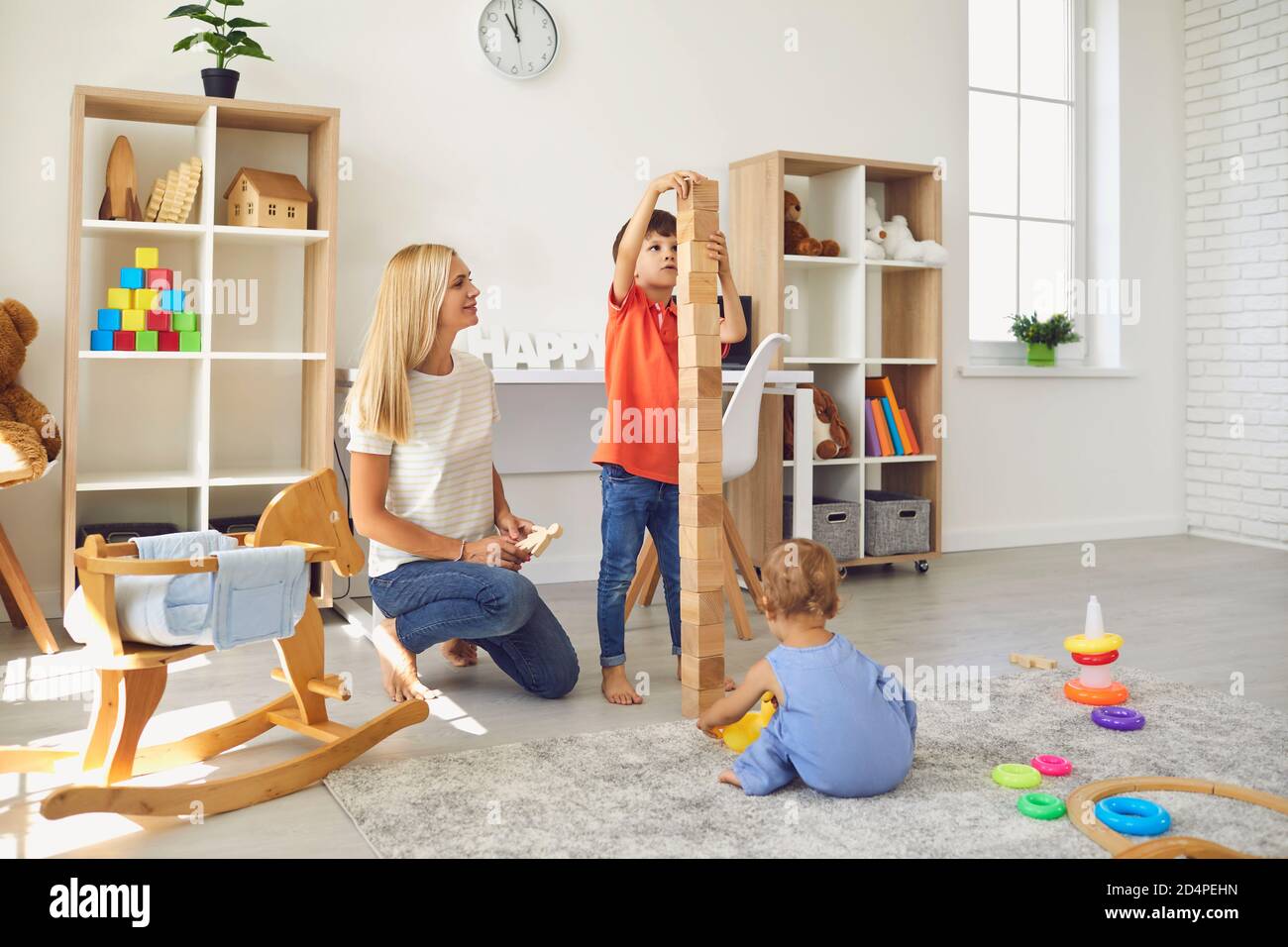 Madre felice con i suoi due bambini che giocano con un sacco di giocattoli e torre a blocchi di costruzione a casa Foto Stock