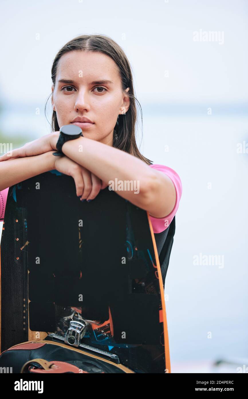 Giovane donna bruna seria con orologio da polso in piedi dietro la tavola da surf Foto Stock