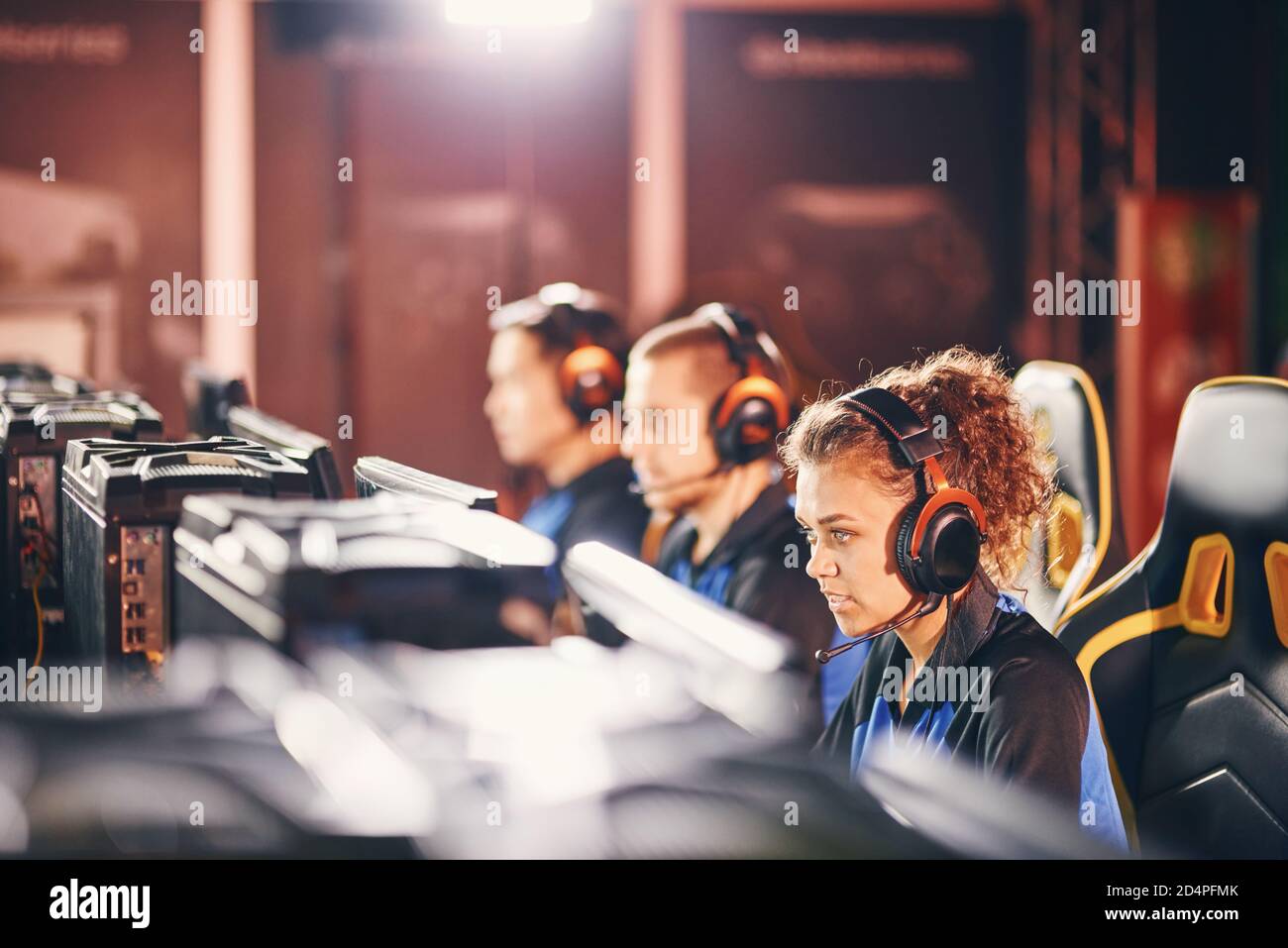 Una giovane squadra di cybersport professionale che indossa le cuffie che partecipano al torneo eSport, che gioca a videogiochi mentre si siede nel club di gioco o internet cafè, si concentra su una ragazza di corsa mixe Foto Stock