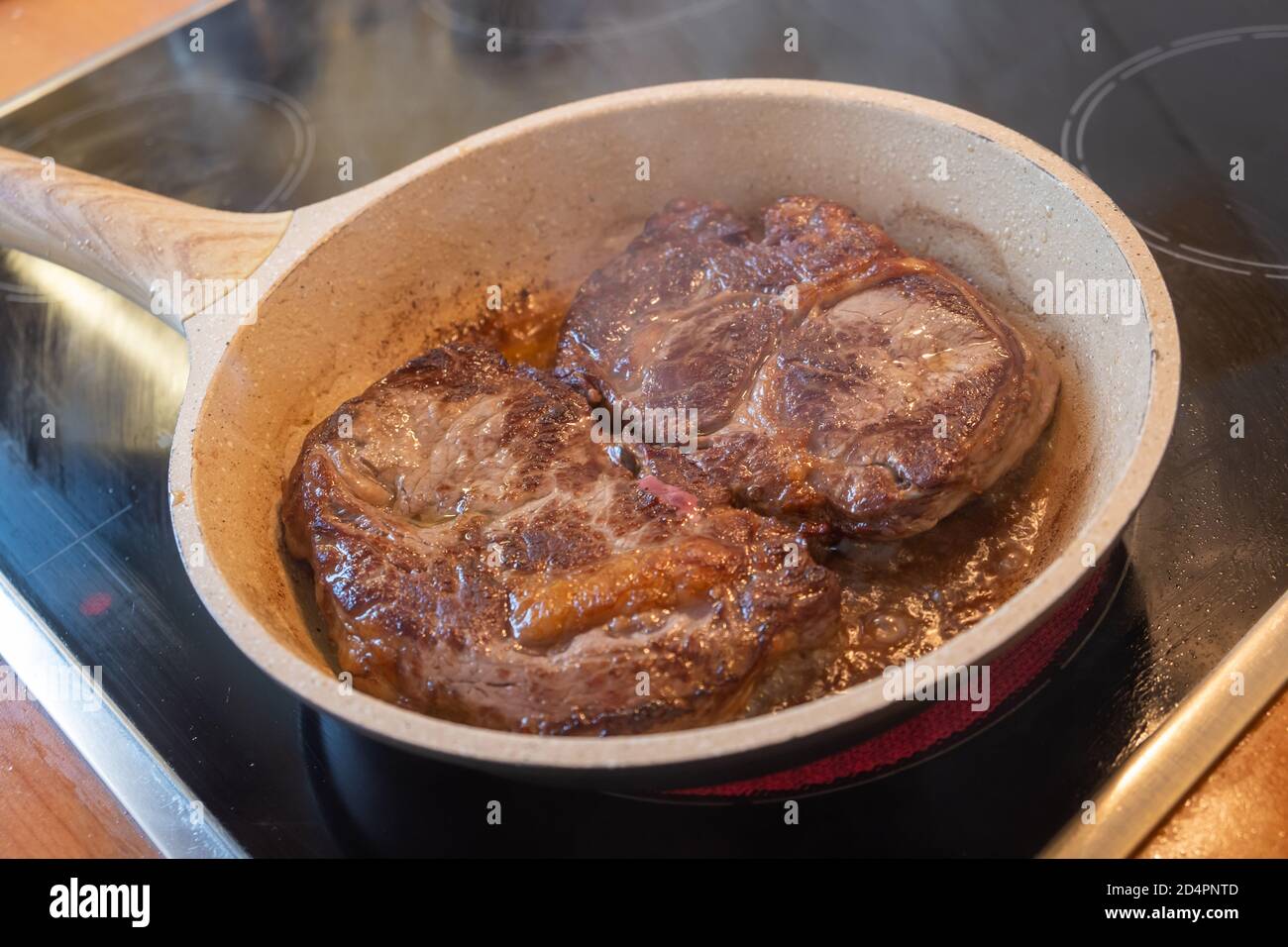 Concetto di carne. Due costolette di maiale fritte in padella di pietra con olio sul fornello. Bistecche brune ben preparate su fette pronte per essere servite. Sfocatura dello sfondo, primo piano Foto Stock