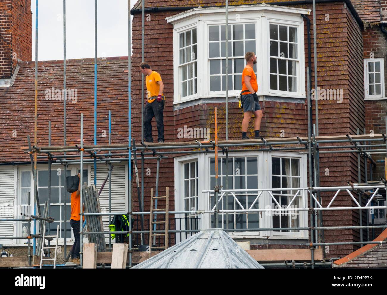 Uomini al lavoro che costruisce impalcature contro una casa. Foto Stock