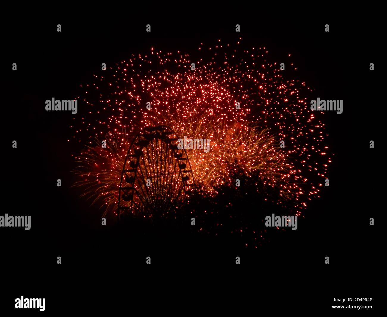 Una ruota di ferro davanti a fuochi d'artificio arancioni e rossi, che illuminano la notte Foto Stock