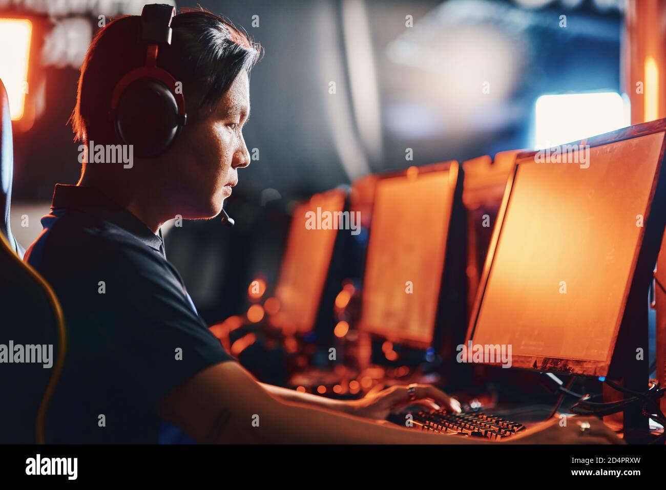 Vista laterale di un ragazzo asiatico focalizzato, un giocatore professionista di cybersport maschile indossando cuffie che gioca online video game, partecipando al torneo eSport Foto Stock