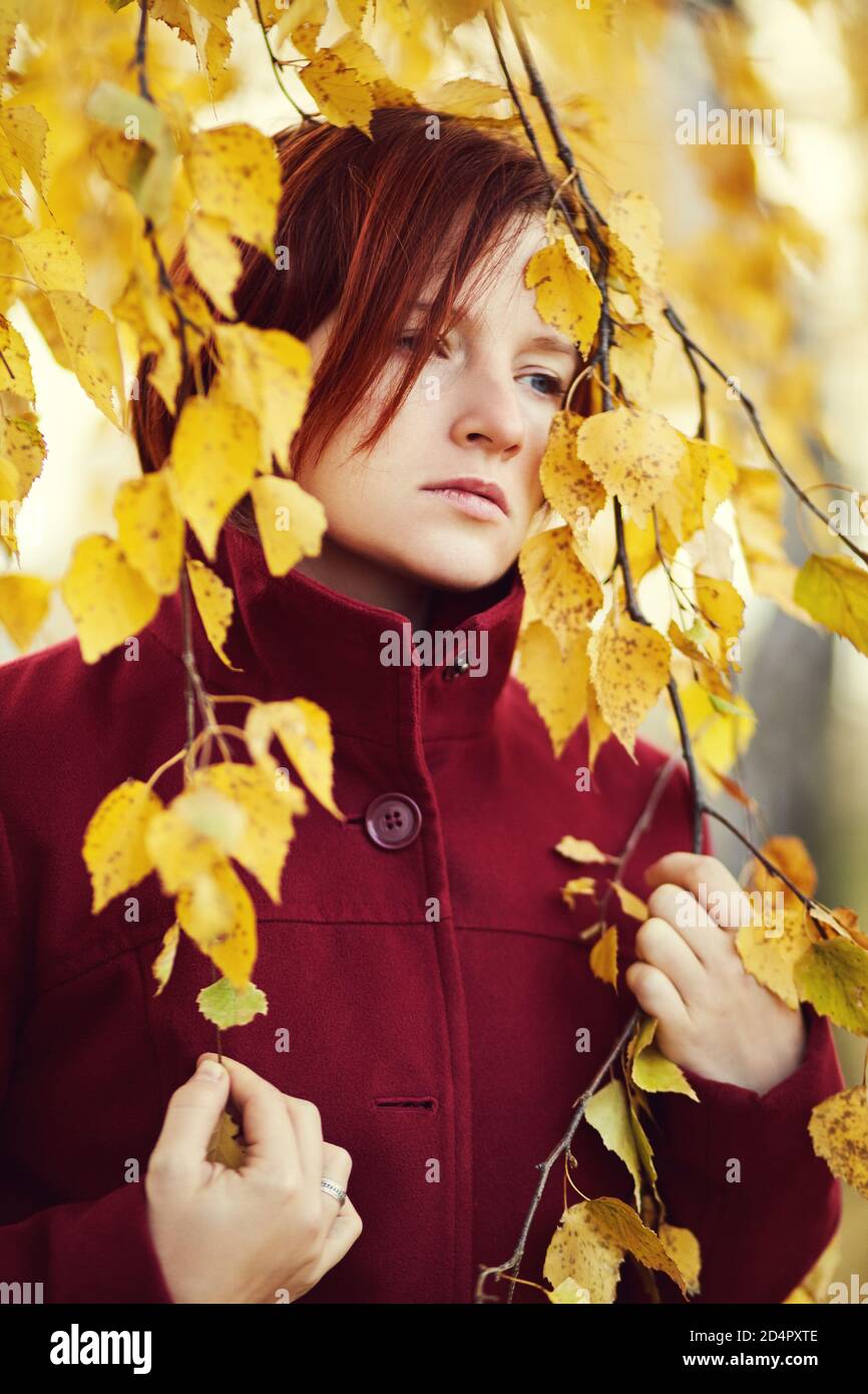 ritratto di una triste donna rossa con foglie gialle in autunno. Foto Stock