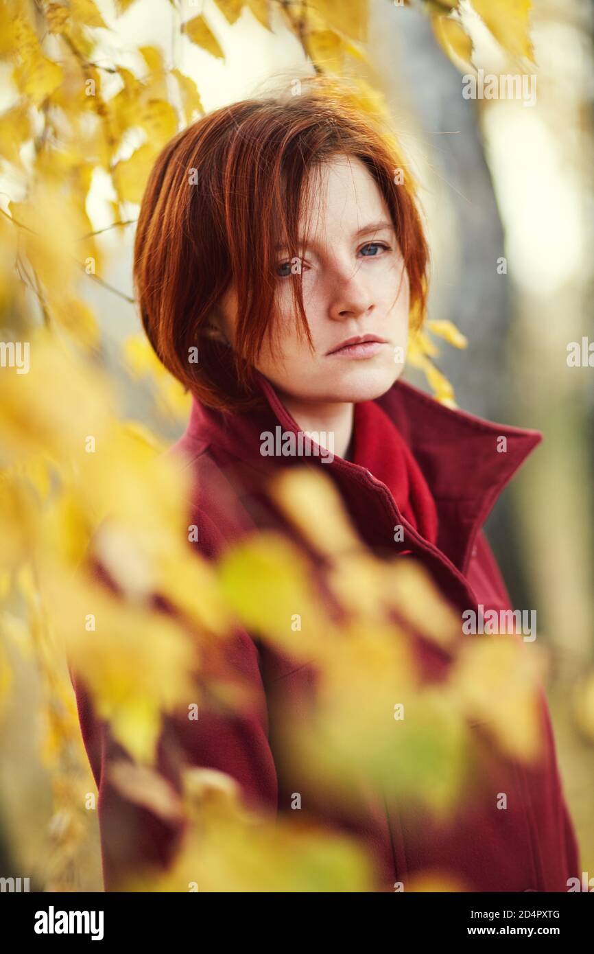 ritratto di una triste donna rossa con foglie gialle in autunno. Foto Stock