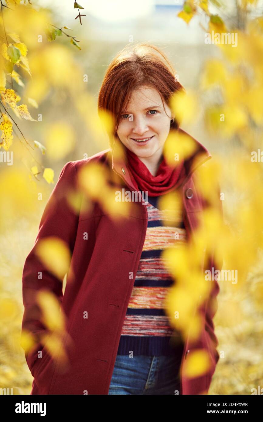 ritratto di una donna sorridente rossa con foglie gialle in autunno. Foto Stock