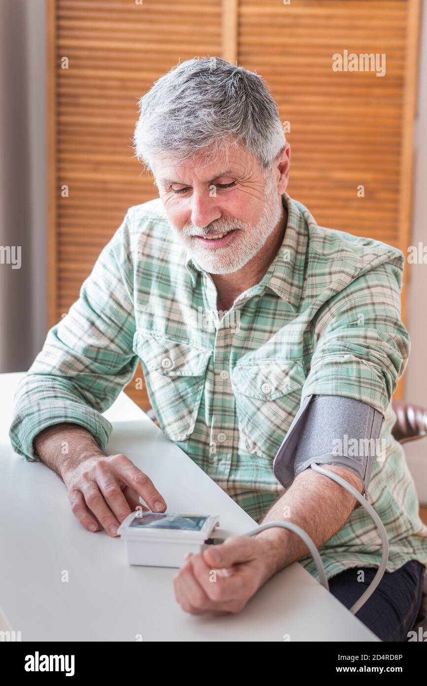 L'uomo prendendo la sua pressione del sangue con un portatile di monitor della pressione del sangue. Foto Stock