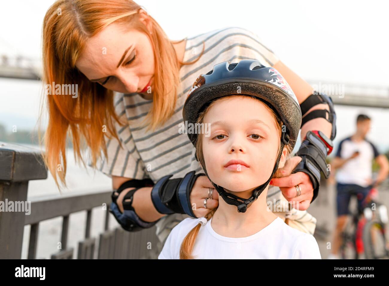 Giovane madre che aiuta la sua piccola figlia a mettere un casco da bicicletta. Ragazza prescolare che ha camminato attivo con sua madre Foto Stock
