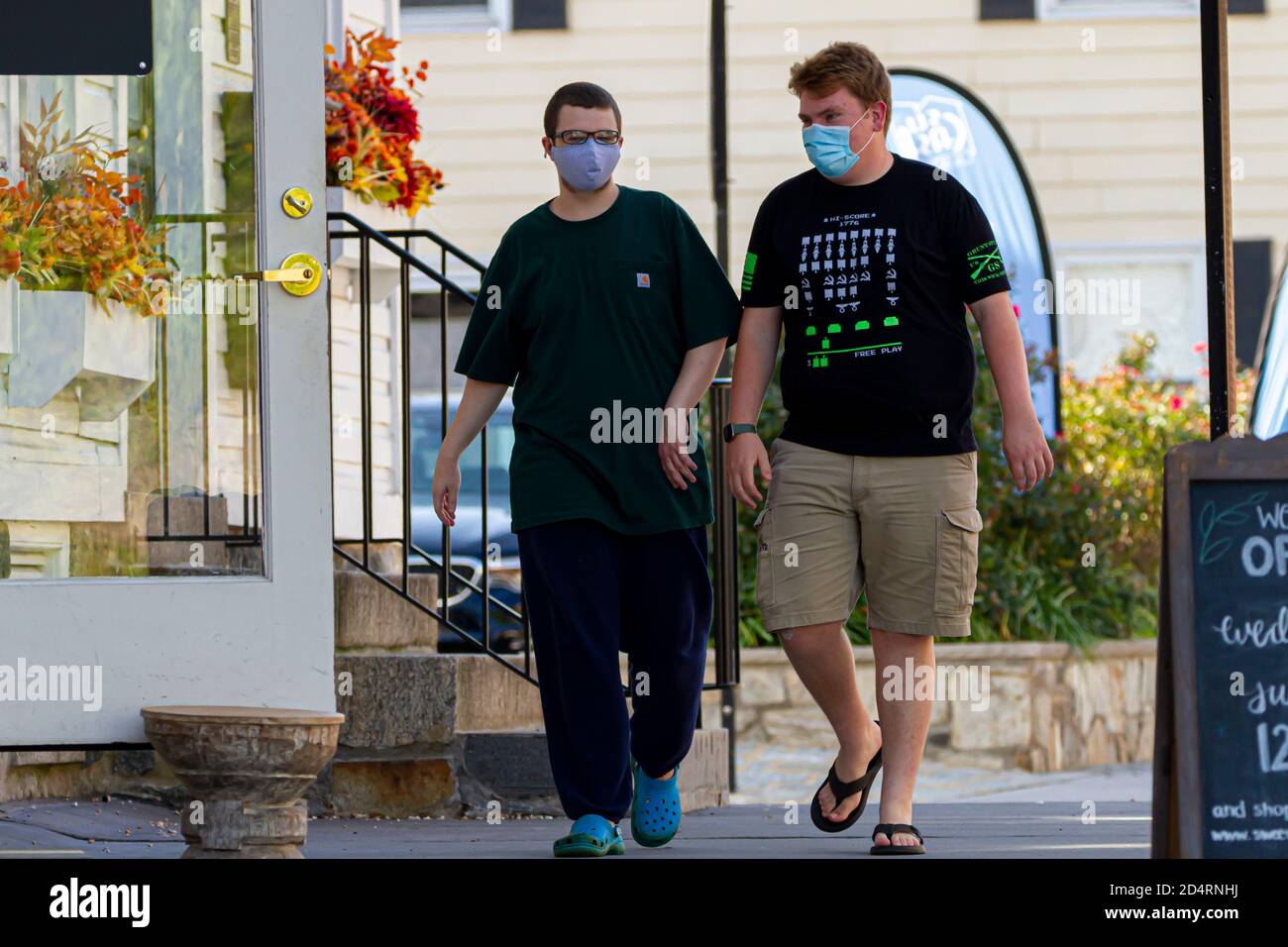 Ellicott City, MD, USA 10/07/2020: Due giovani uomini che indossano maschere per il viso a causa di COVID-19 sono a piedi in strada. Hanno outfit estivo casual. Co Foto Stock