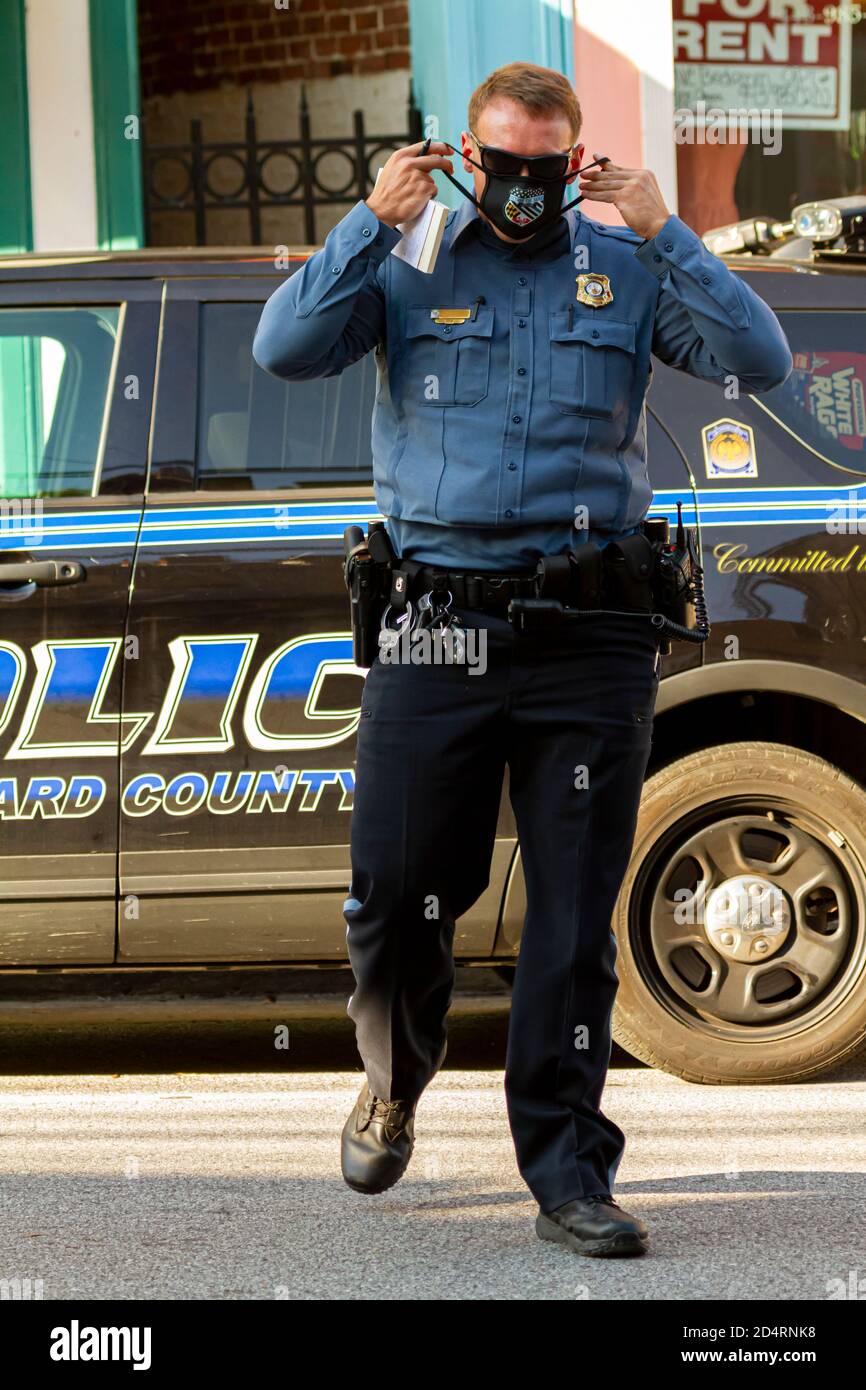 Ellicott City, MD, USA 10/07/2020: Un giovane poliziotto caucasico maschio sta attraversando la strada. Sta mettendo sulla sua maschera nera mentre cammina Foto Stock
