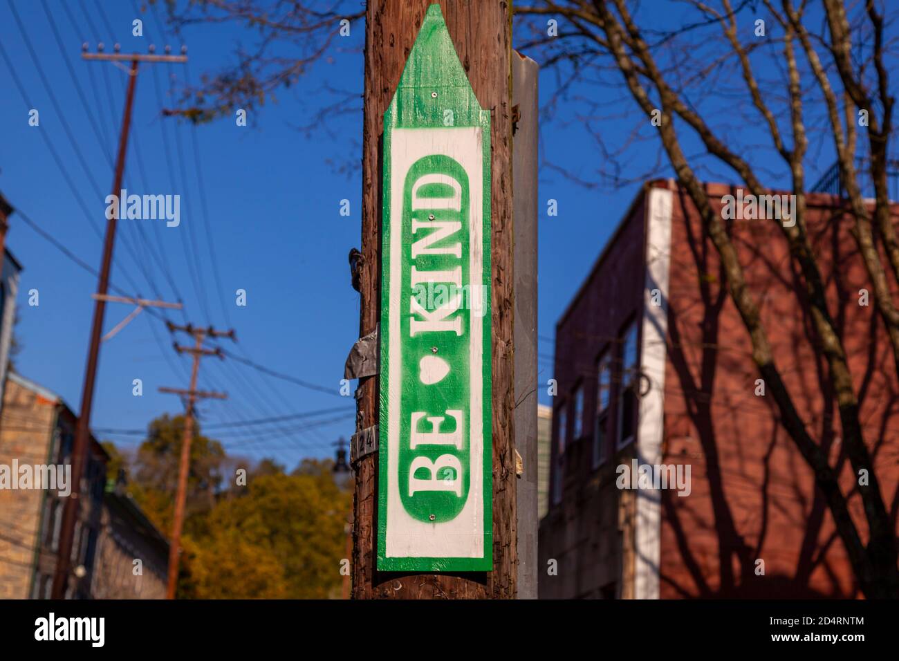 Un cartello anonimo in legno a forma di freccia rivolta verso l'alto che è attaccato ad un palo telefonico a Ellicott City, MD. Il segno dice 'SIA GENTILE) con un symb del cuore Foto Stock