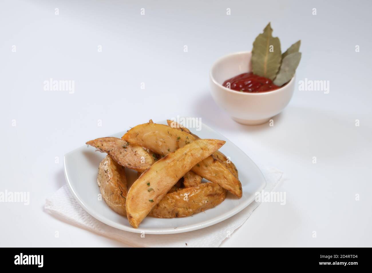 Rustica o stile di paese Erba patate fritte su un piccolo Piatto con salsa al barbecue su una superficie bianca Foto Stock