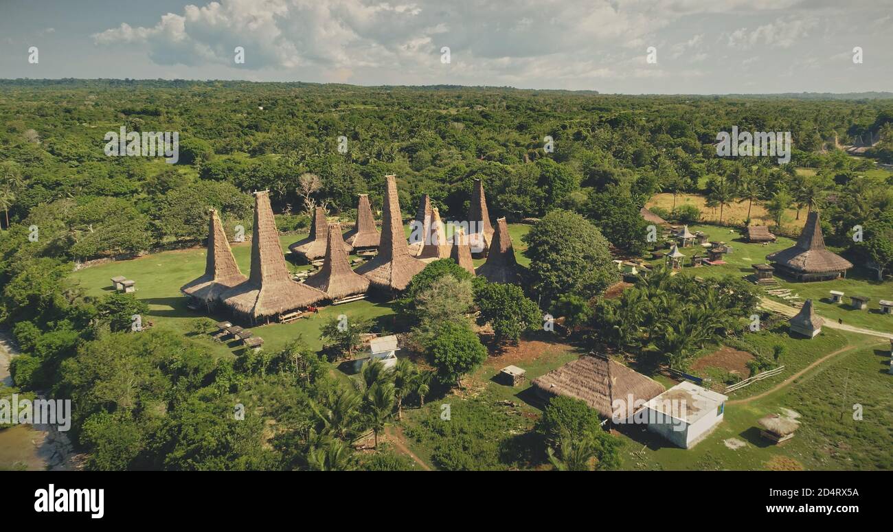 Piccole case tradizionali a valle verde e spiaggia di sabbia vista aerea. Incredibile natura della campagna indonesiana di un villaggio di lunga tradizione. Animali fienile vicino tetti ornati edificio a Sumba Island, Asia Foto Stock