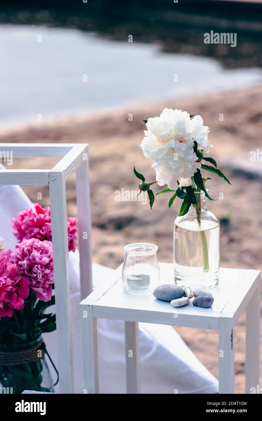 Primo piano dettagli di matrimonio o di festa con peonie in un vaso di vetro vicino al mare. Foto Stock