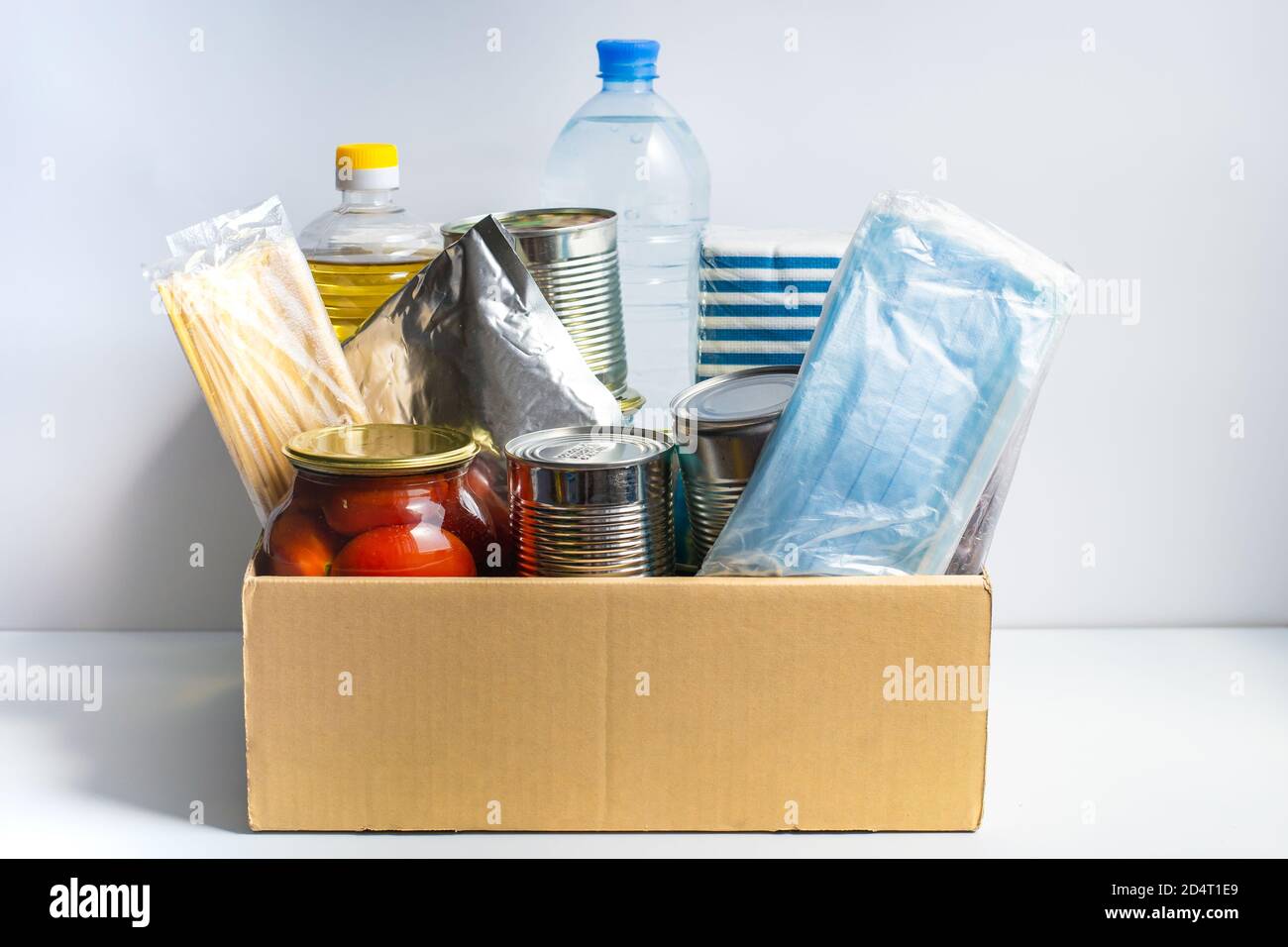 Scatola con cibo per una donazione di beneficenza. Cibo in scatola, pasta, cetrioli sottaceto, olio vegetale, tè. Tovaglioli di carta, maschere di protezione. Consegna di cibo. Foto Stock